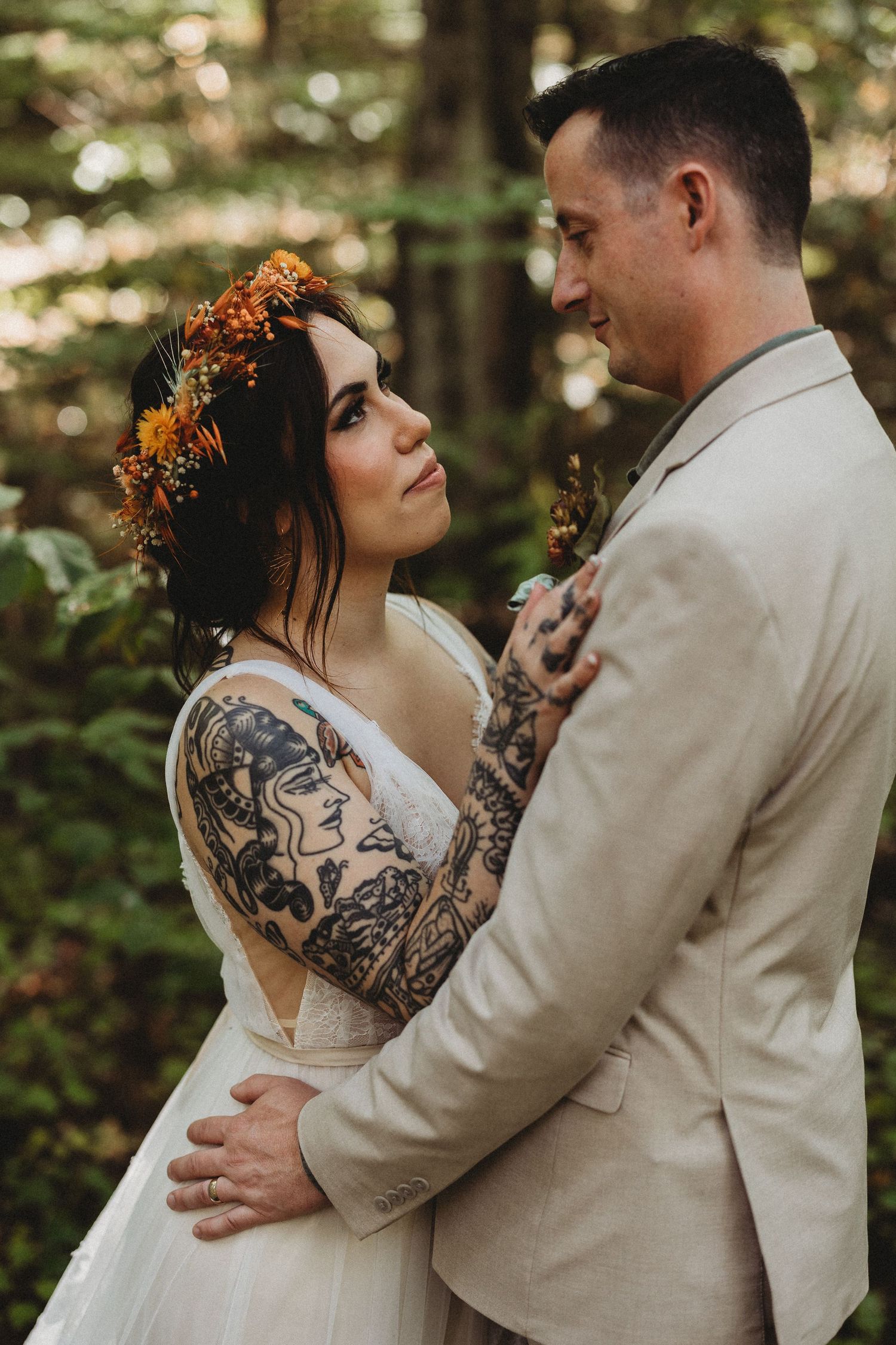 Romantic forest wedding couple in beige suit and white dress with tattoos share intimate moments during photo session.