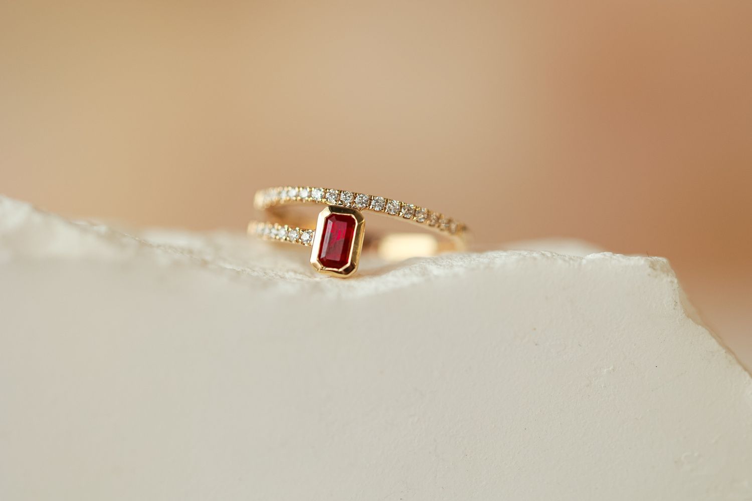 Elegant gold rings with gemstones arranged on beige textured surface.