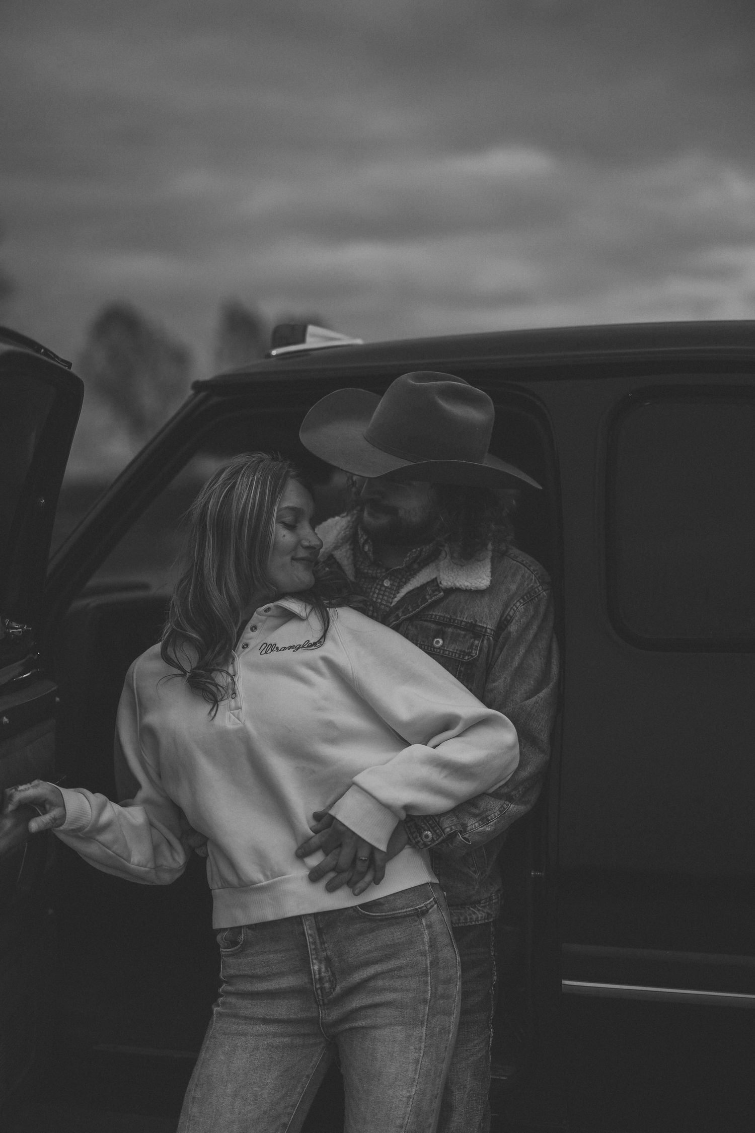 A couple sharing an intimate moment in a car with a moody black and white aesthetic.