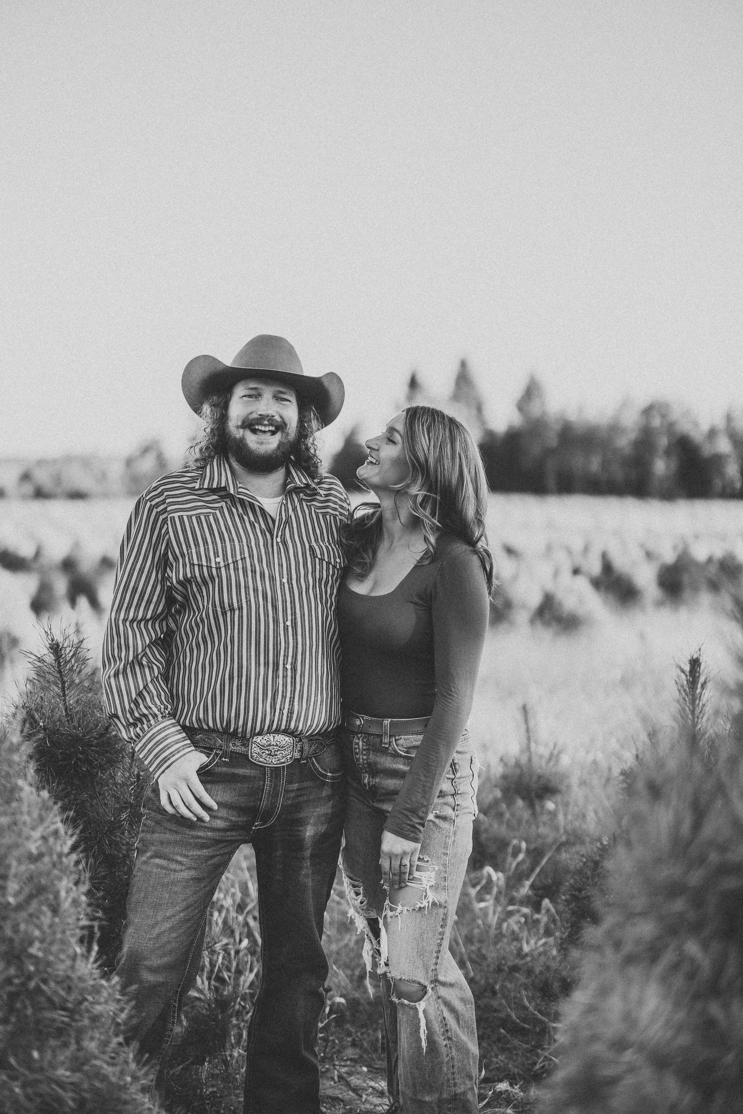 A couple shares a tender moment together in a rustic outdoor setting with tall grass and natural scenery.