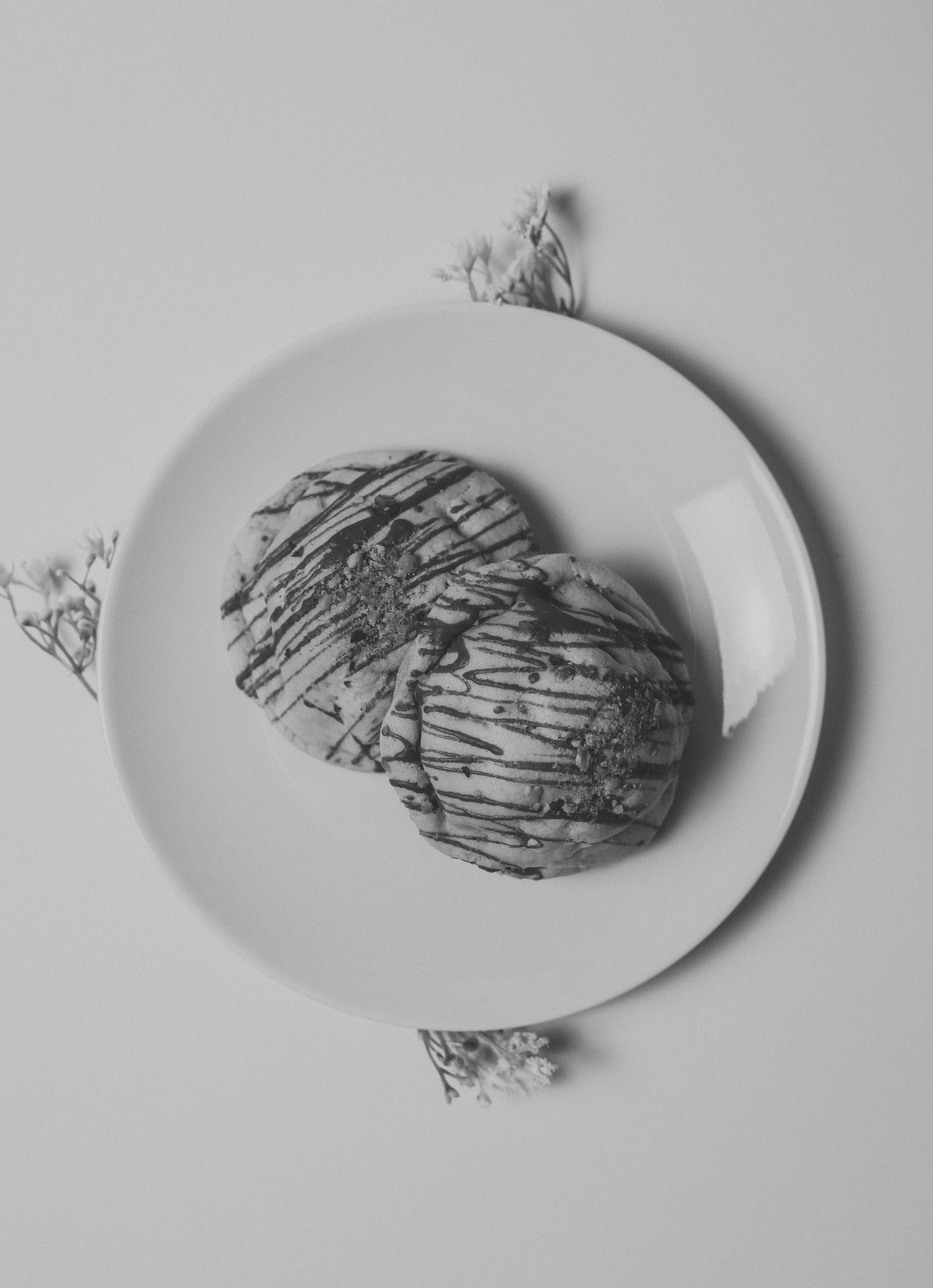 Black and white close-up of chocolate drizzled cookie on white plate with delicate flowers.