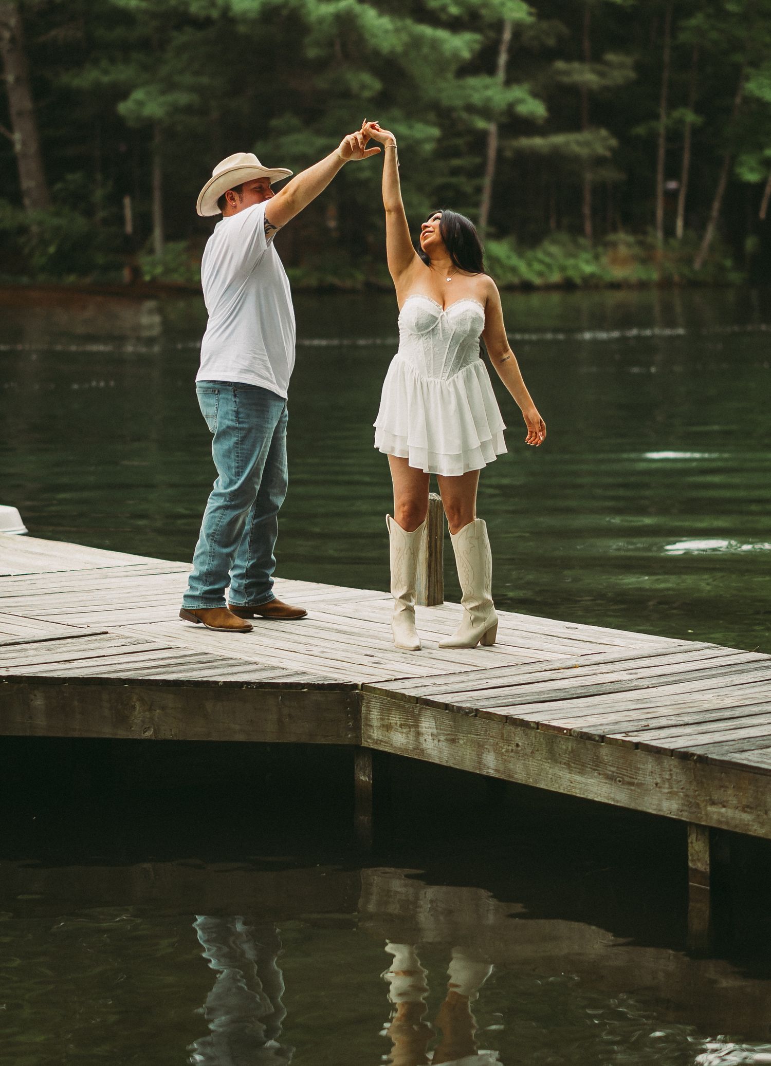 Couple holding hands while walking on wooden dock over serene lake.