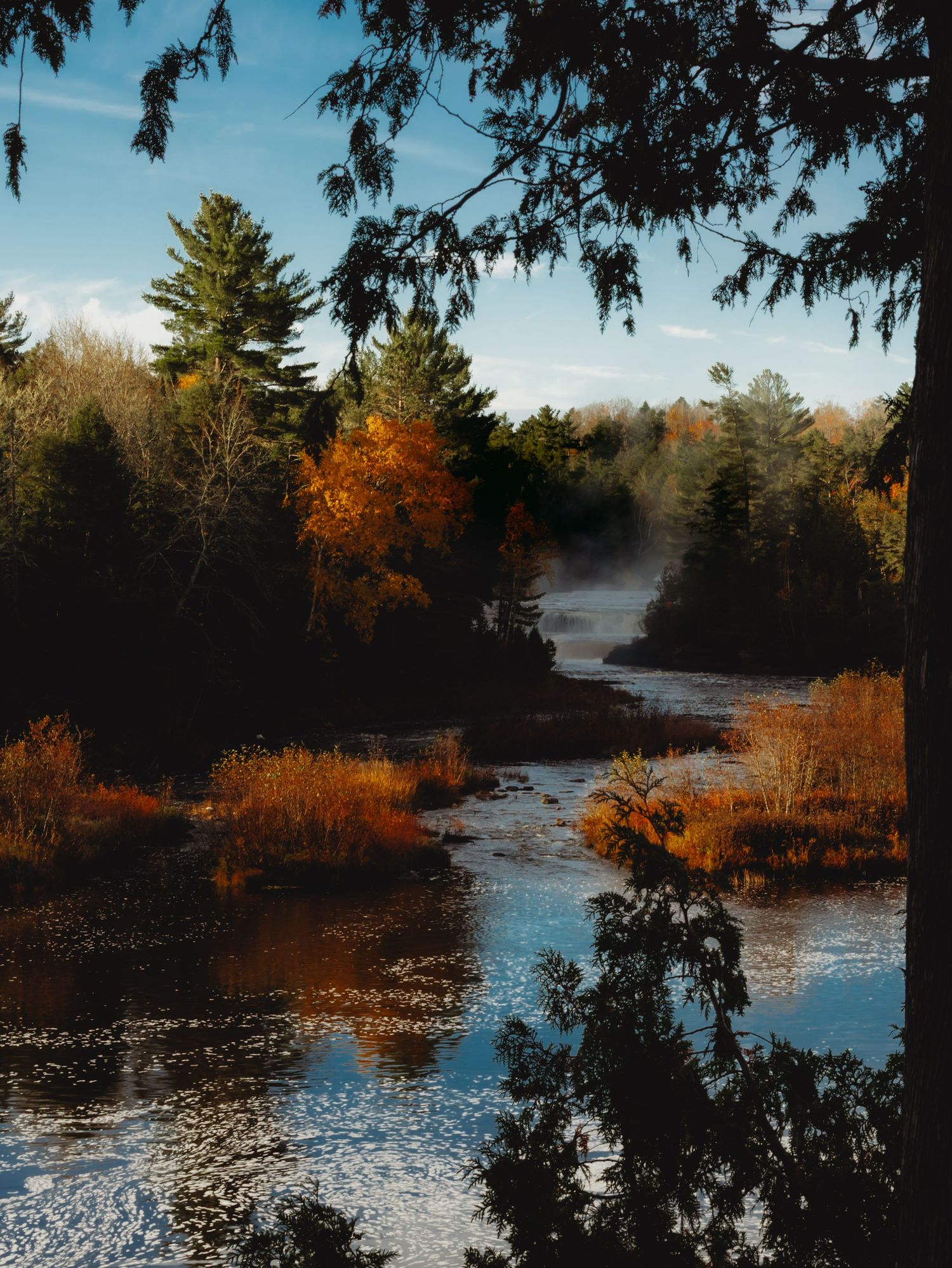 Misty lake landscape with fall colors reflecting in calm waters.