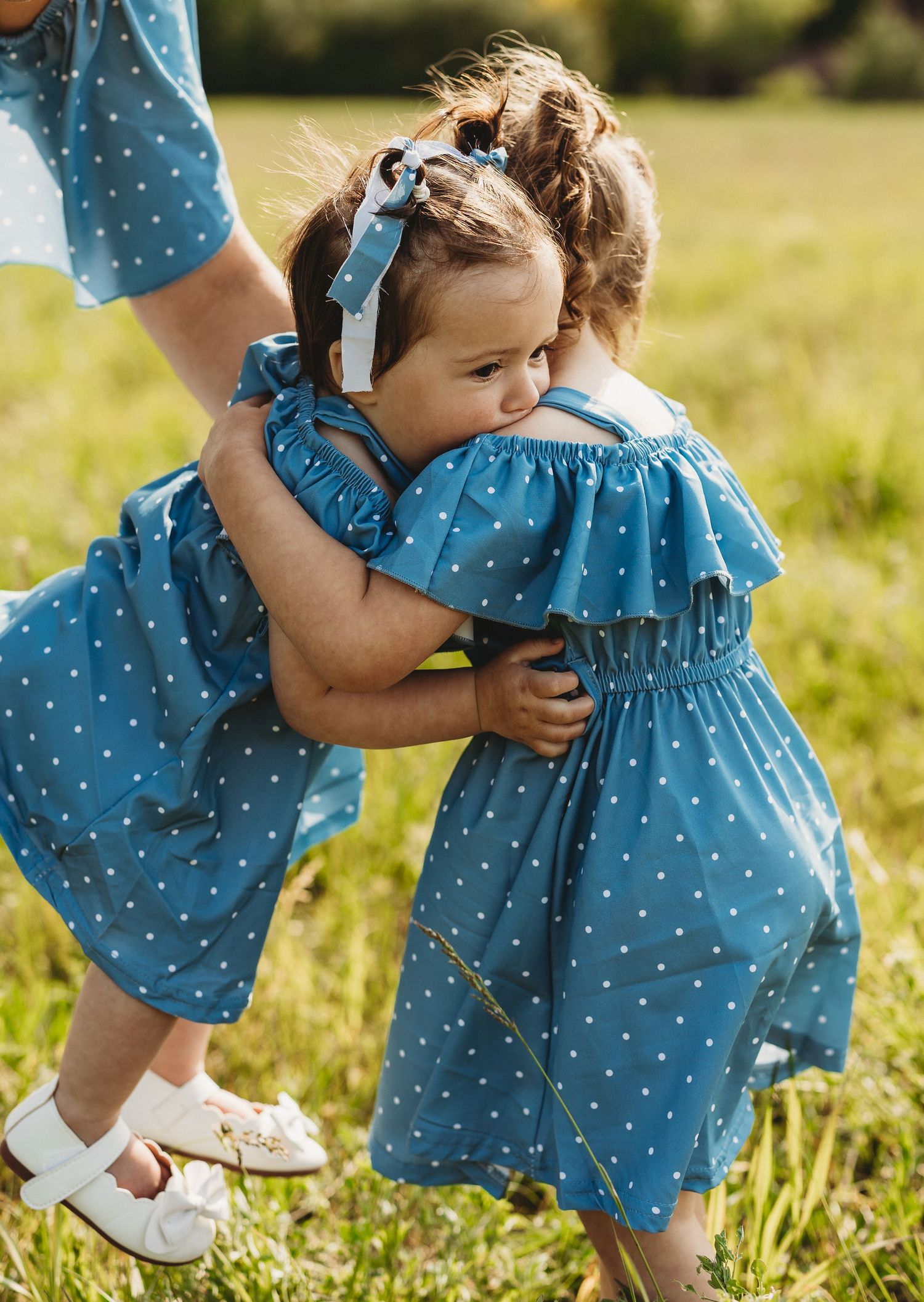 Close-up shots of matching polka dot blue dresses in a sunny meadow with white shoes and summer fashion details.