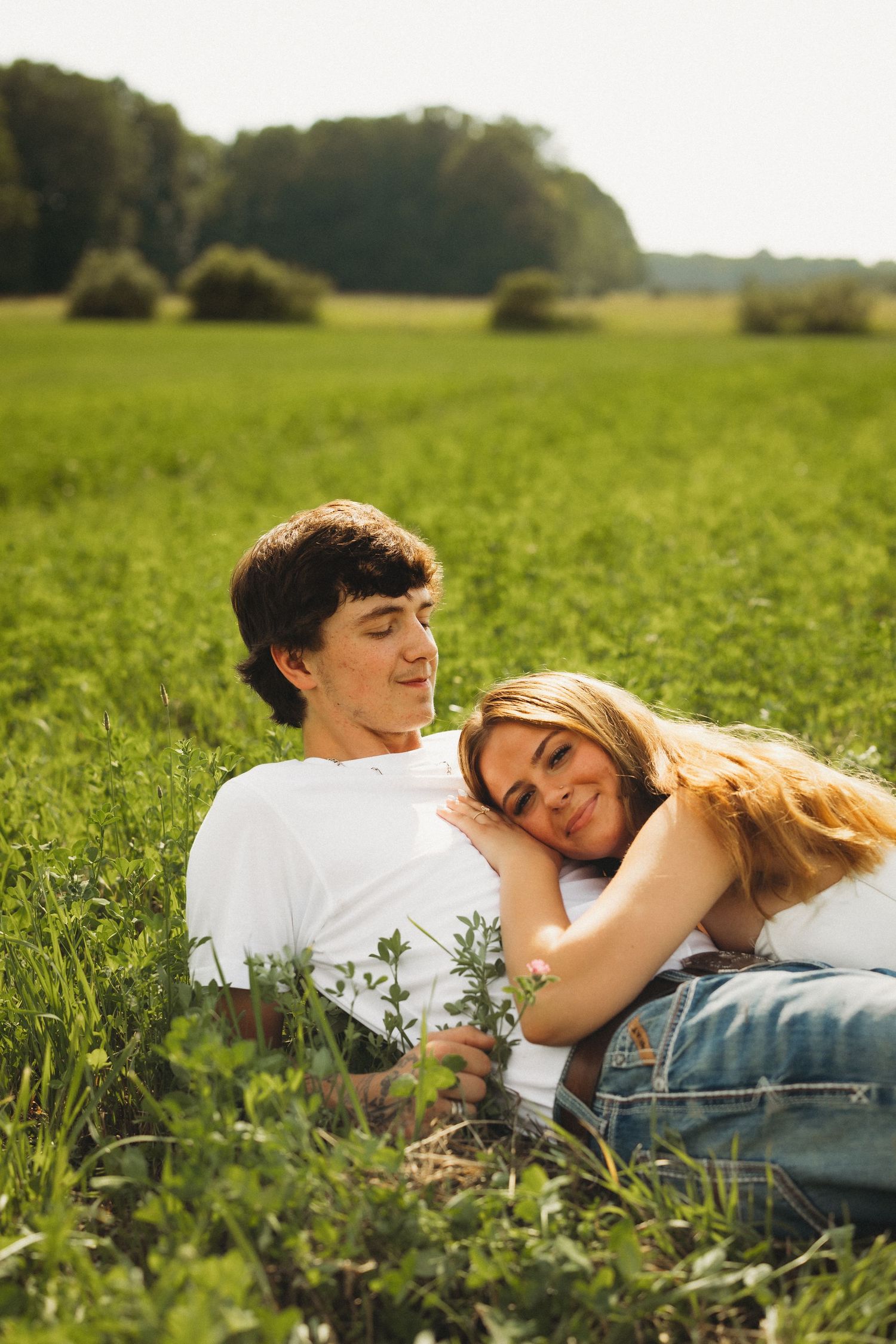 Young couple relaxing together in a lush green field on a sunny day, smiling peacefully.