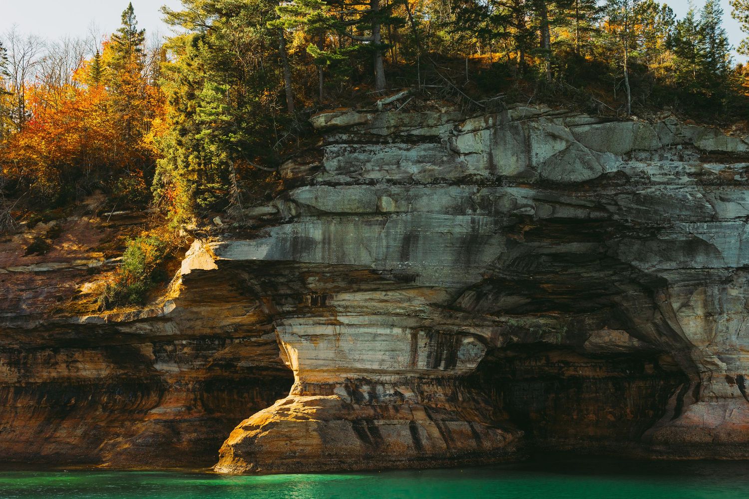 Sun-lit limestone cliffs with autumn trees perched along the rocky ledge.