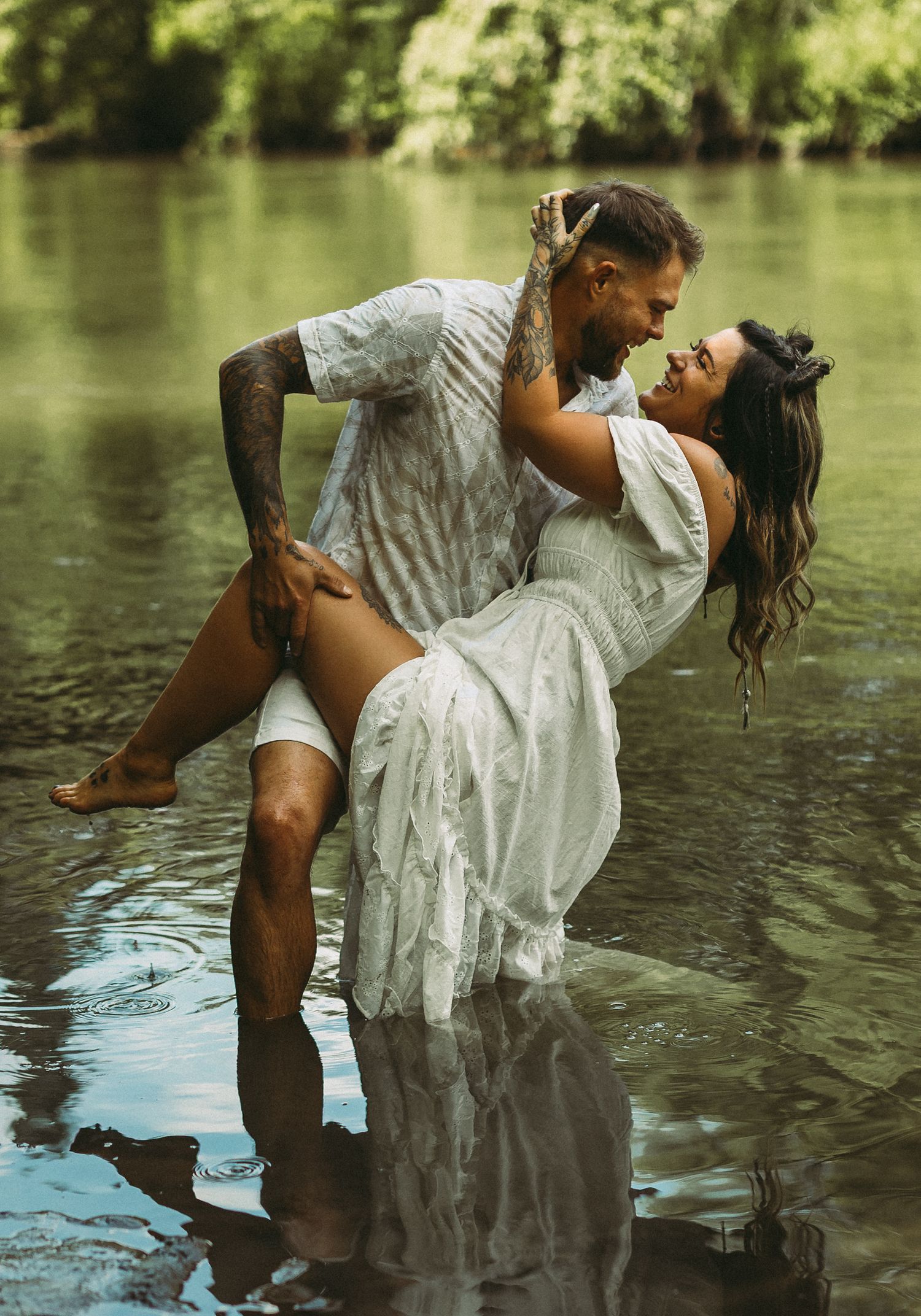 Playful couple in white clothing dancing and splashing in shallow water.
