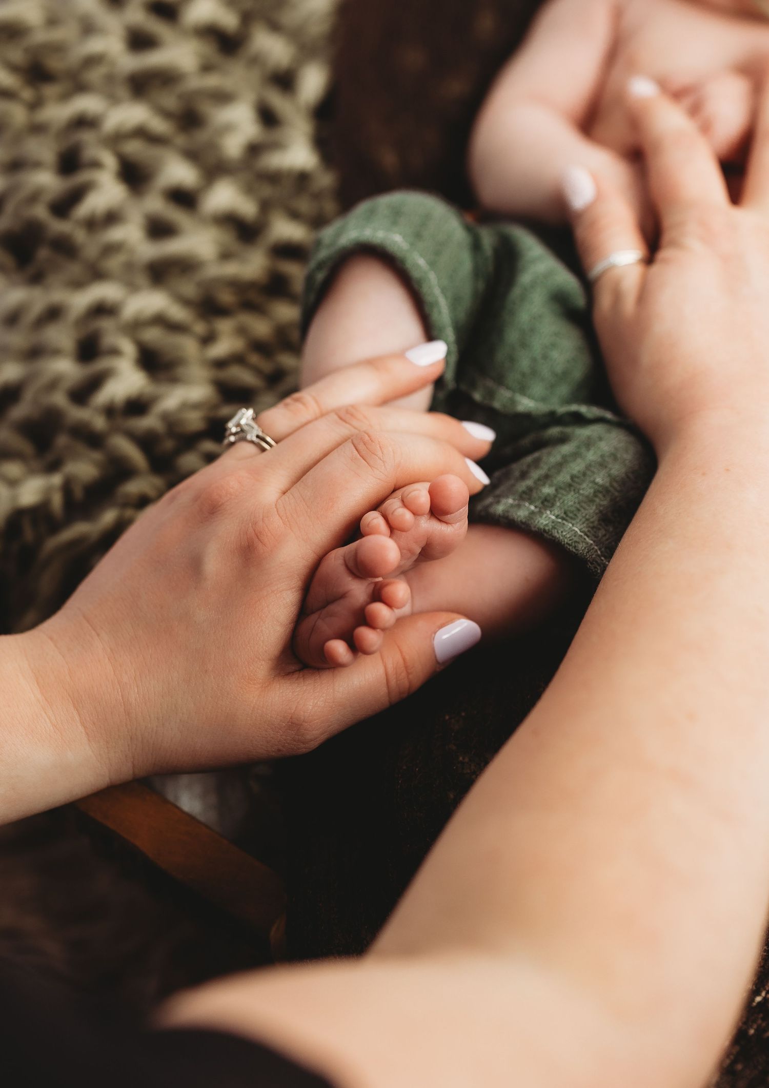 Close-up shots of gentle hands holding tiny newborn fingers against a textured background.