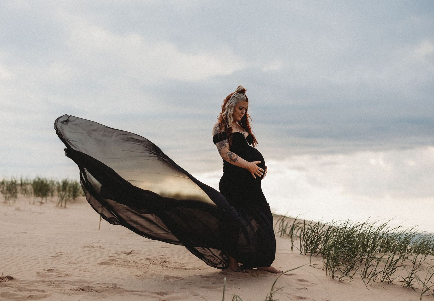 Dramatic maternity photo with flowing black dress on windy beach.