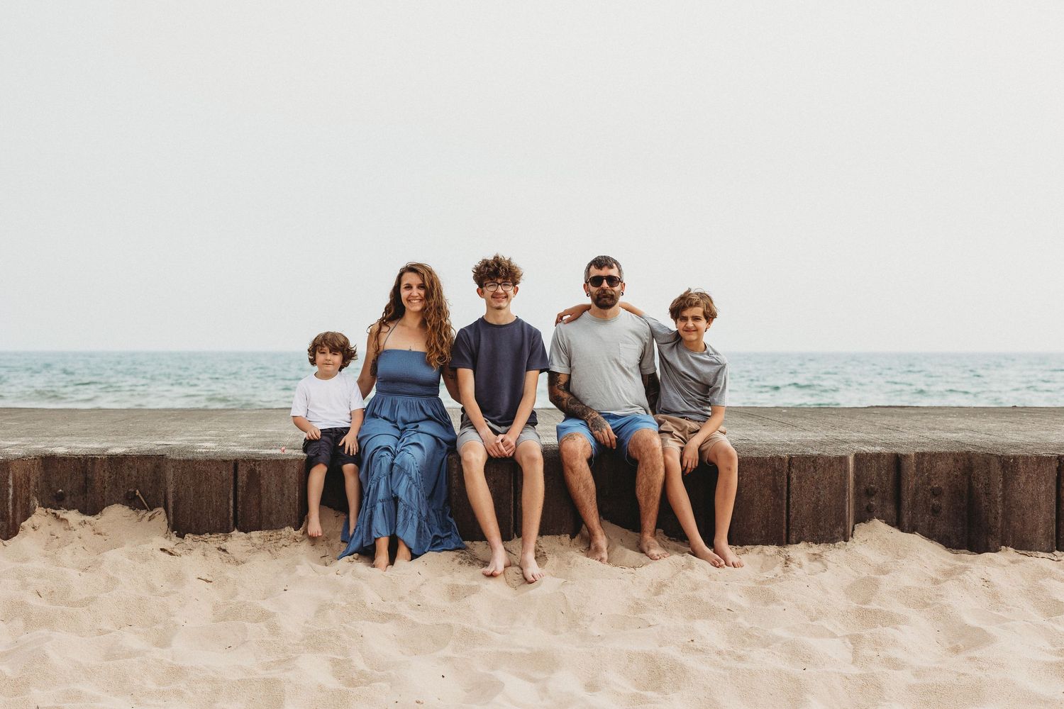 A family sitting together on a concrete barrier at the beach with ocean waves behind them.