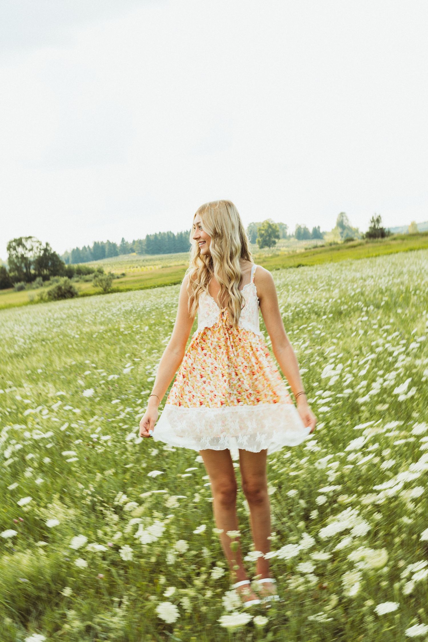 A summer dress-clad figure standing in a field of white wildflowers on a bright sunny day.