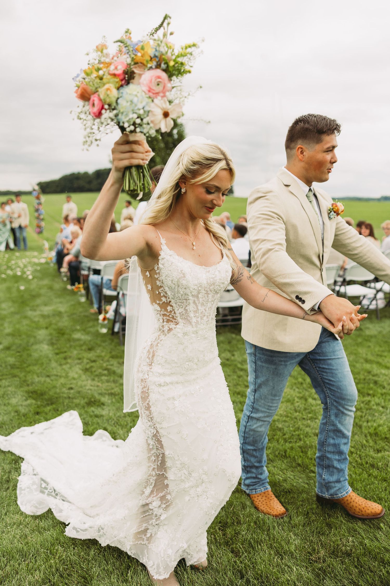 Newlyweds dance and celebrate on a green lawn at outdoor wedding reception.