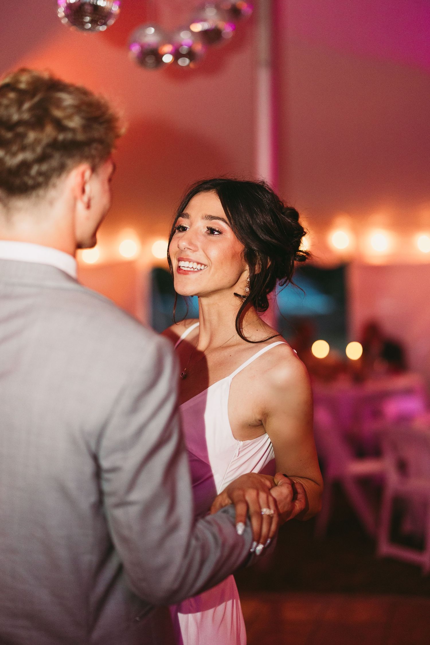 Couple dancing together under pink disco lights at wedding reception.