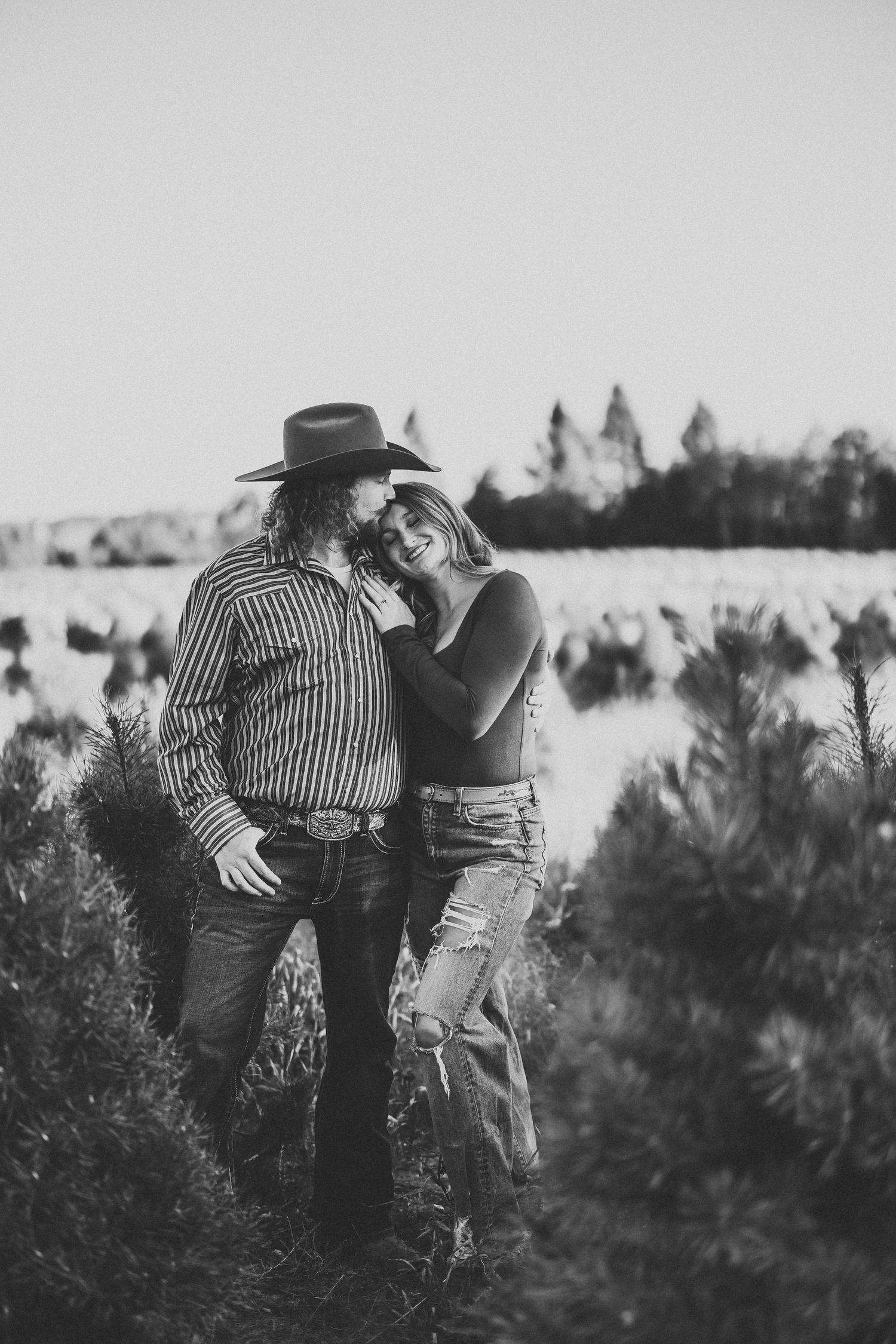 Black and white photo series showing a couple in western attire embracing in a field of evergreen trees.