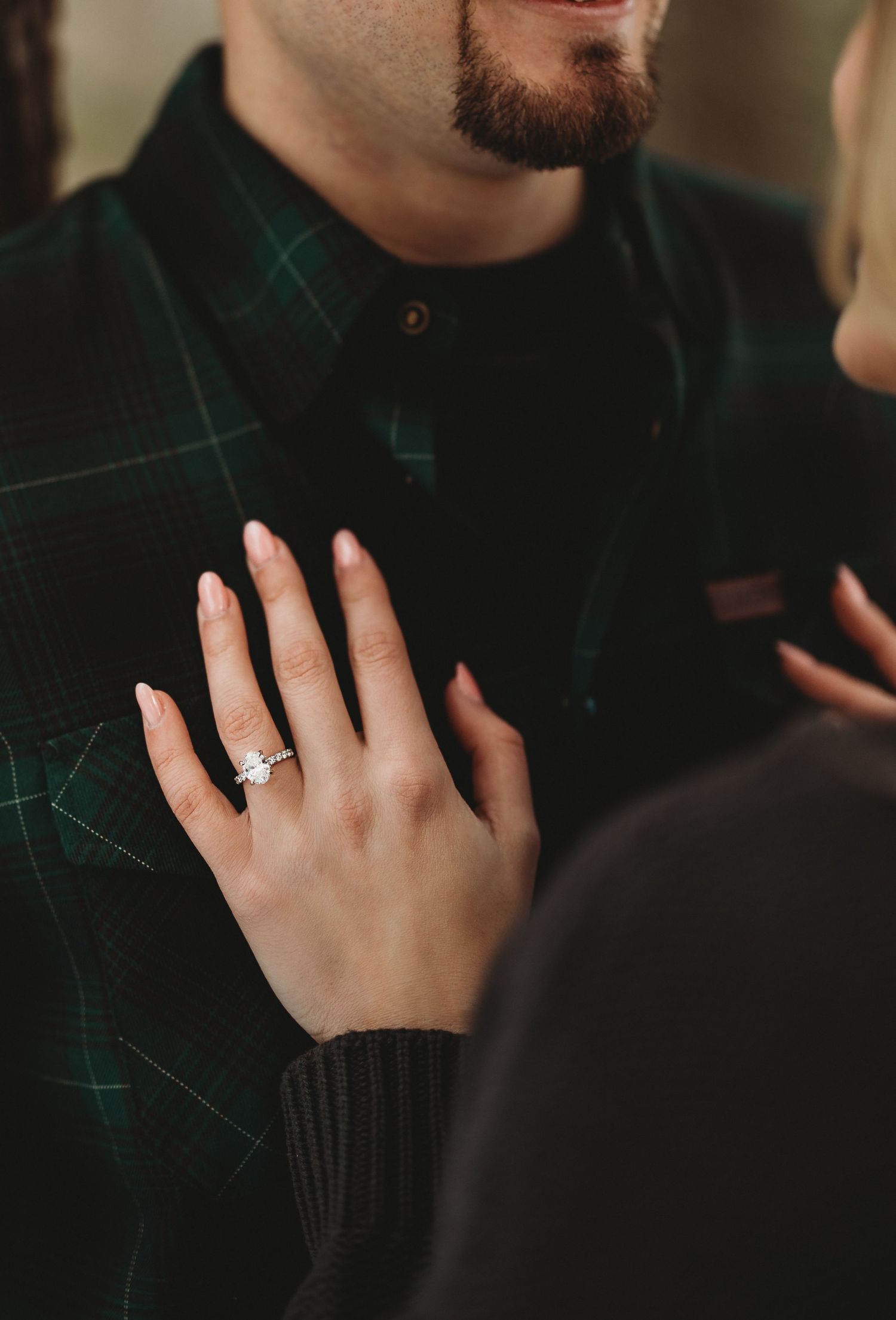 Close-up sequence showing an engagement ring on a hand against a dark green sweater background.