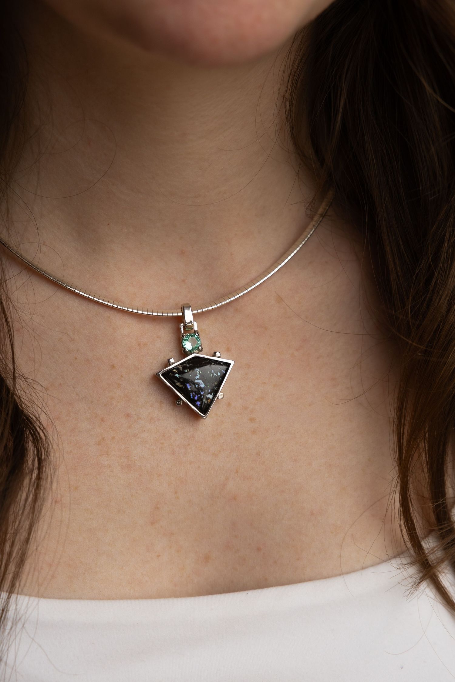 Handcrafted silver pendant necklace with a triangular dark stone and small turquoise accent, worn on a slim silver collar chain.