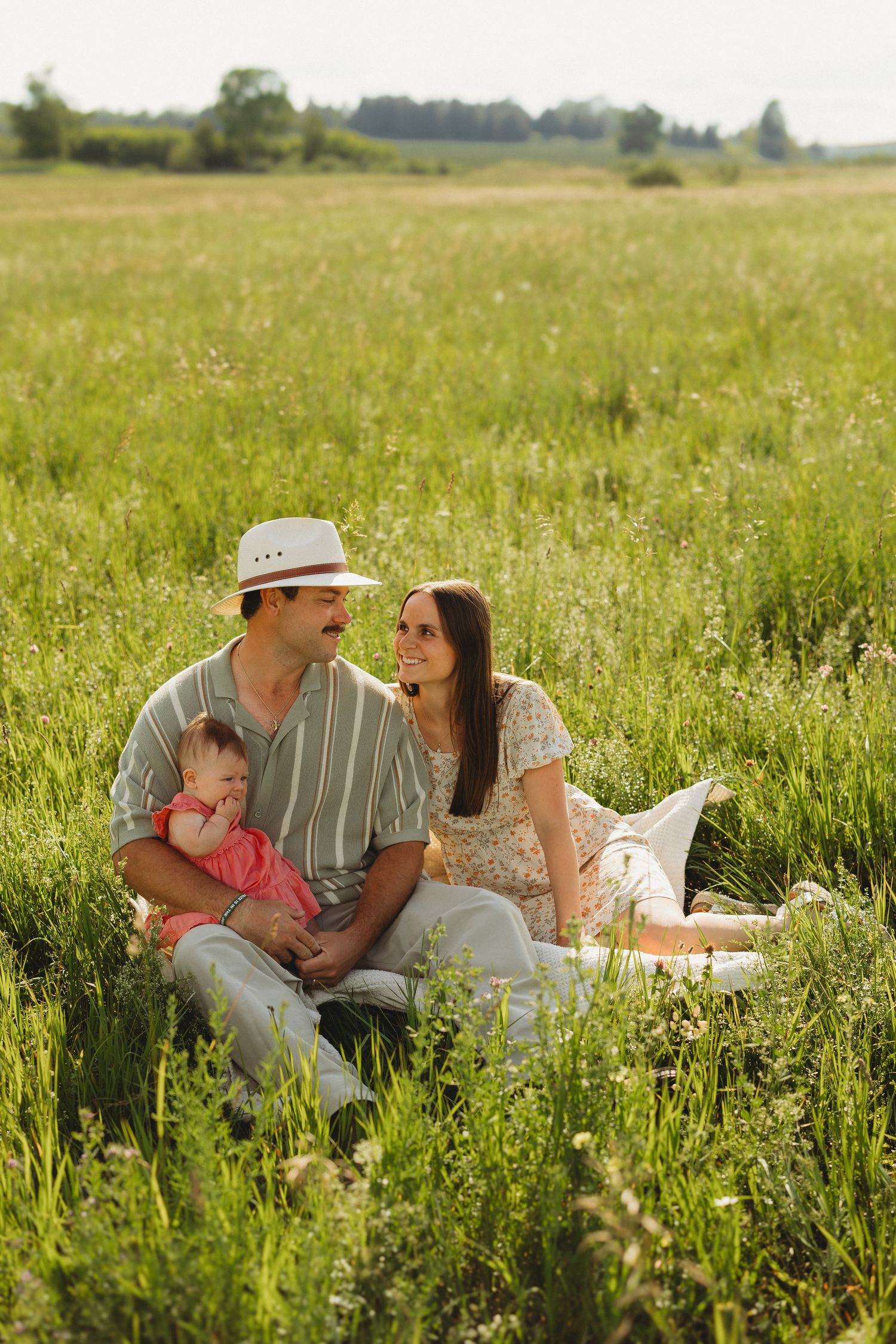 Happy young family with baby sitting in green summer field enjoying a sunny day outdoors.