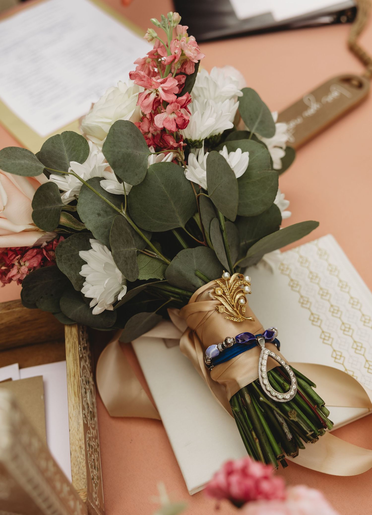 Elegant bridal bouquet with pink, white flowers and eucalyptus, wrapped in gold ribbon with blue bracelet charm.