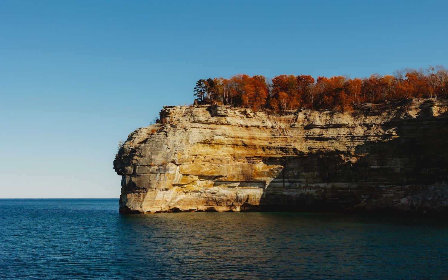 Rocky limestone cliffs rising from turquoise waters with autumn foliage on top.