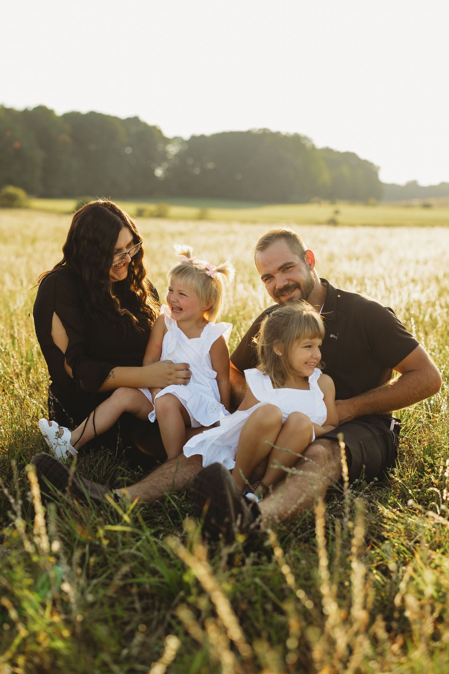 Family enjoying intimate moments together while sitting in a sun-drenched field.