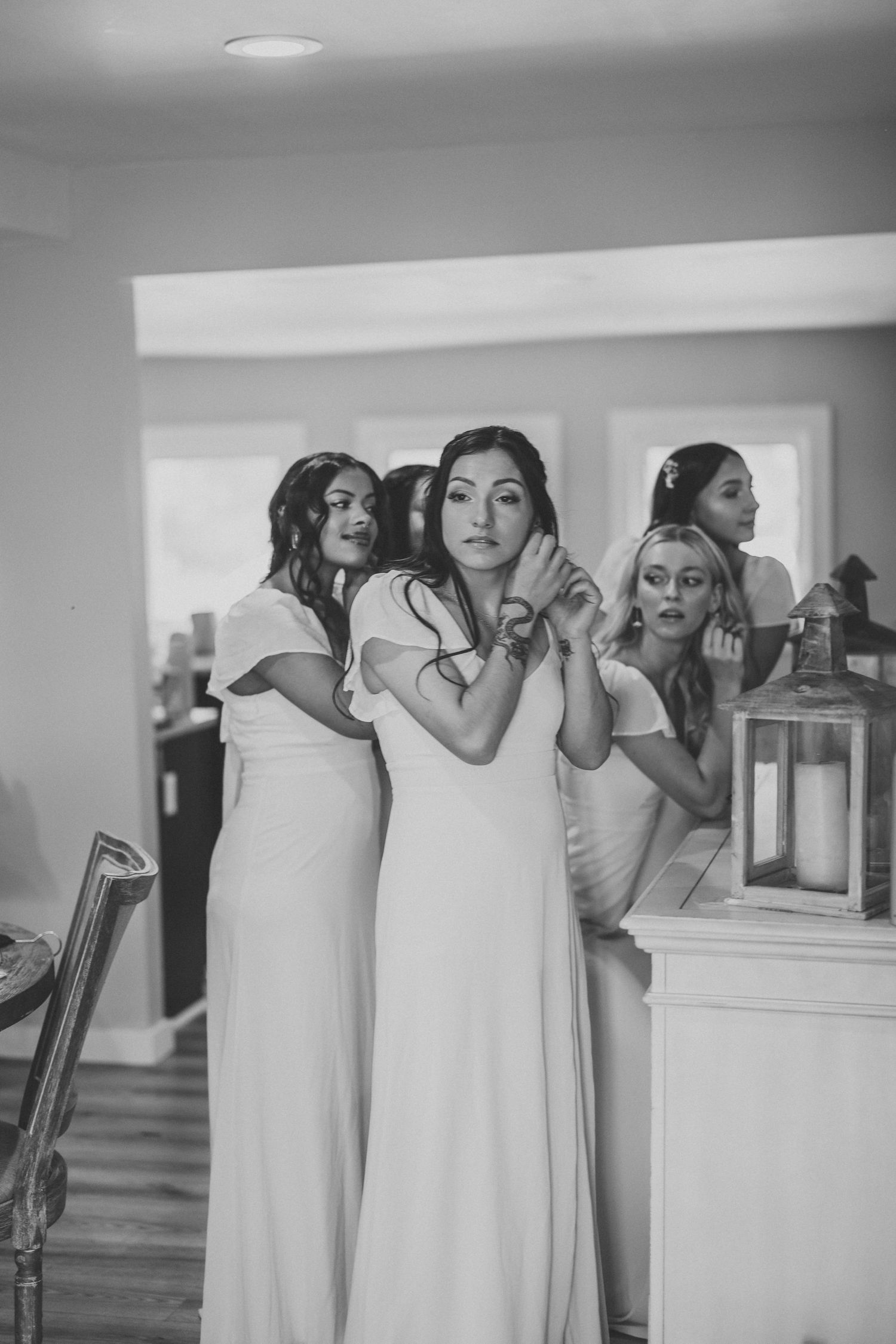 Bridesmaids in white dresses prepare for a wedding ceremony while getting ready in a brightly lit room.