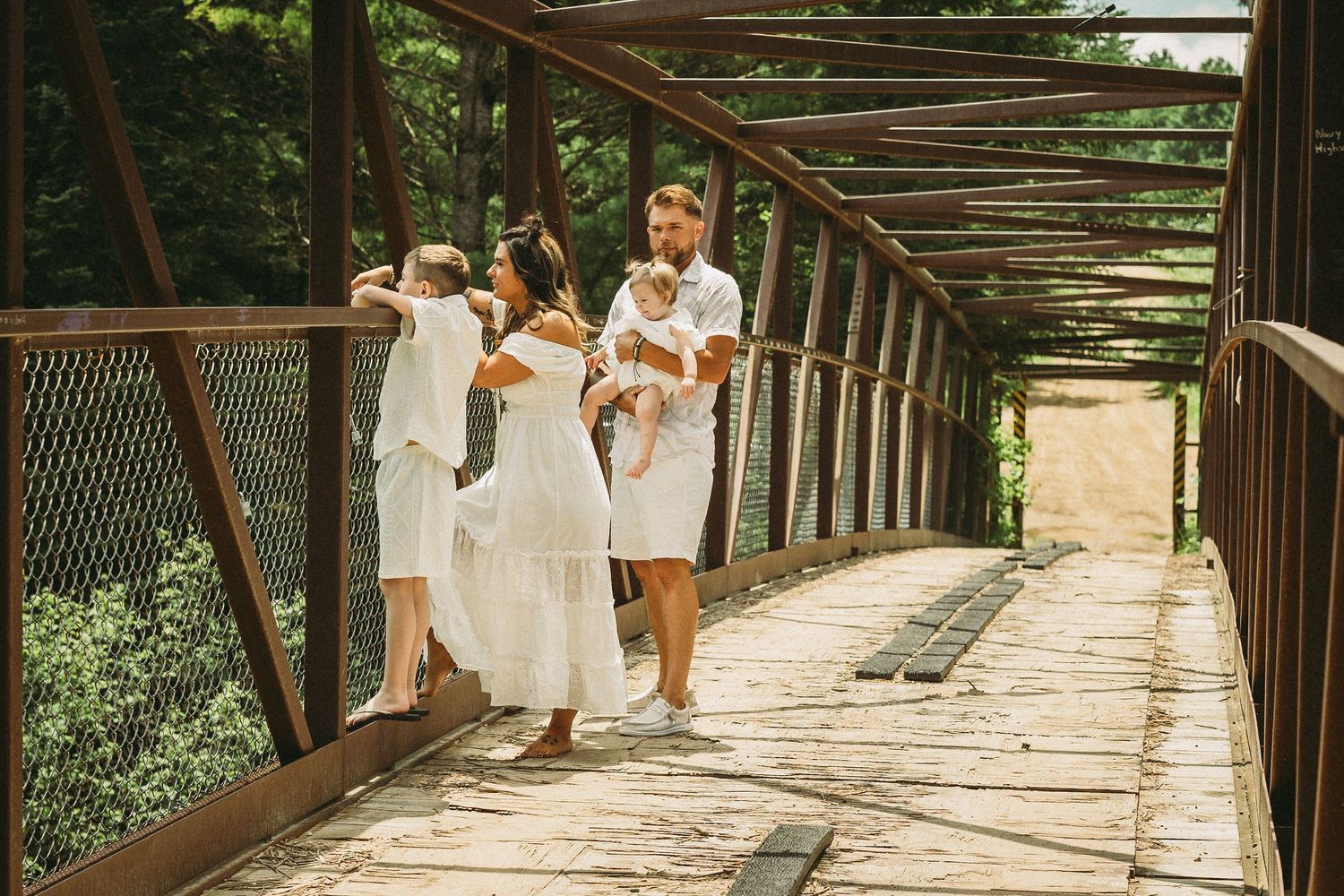 A group wearing white outfits walks across a rustic wooden bridge surrounded by lush greenery.