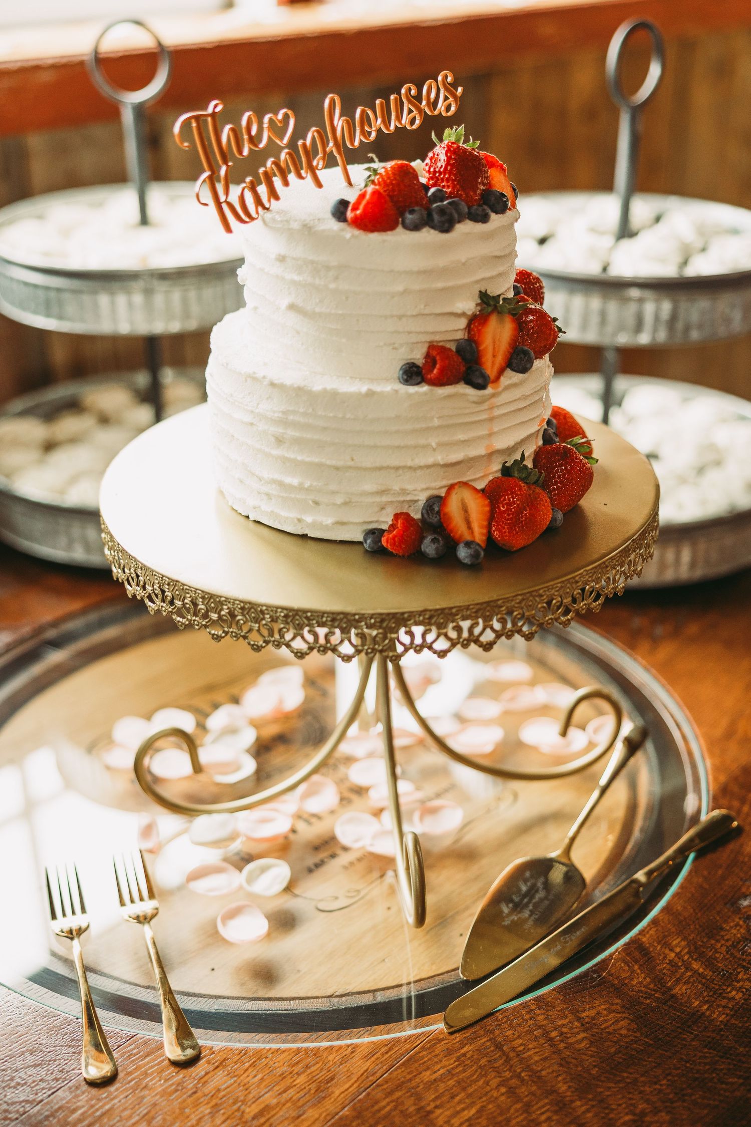 White two-tier wedding cake decorated with fresh strawberries and berries on an ornate metal cake stand.