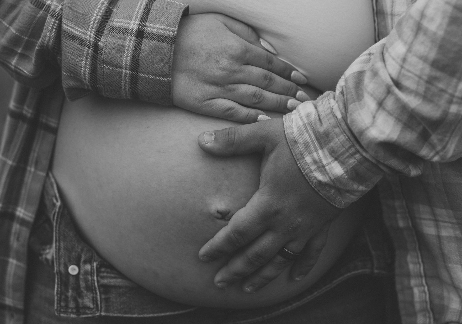 Black and white maternity photo with gentle hands cradling baby bump.