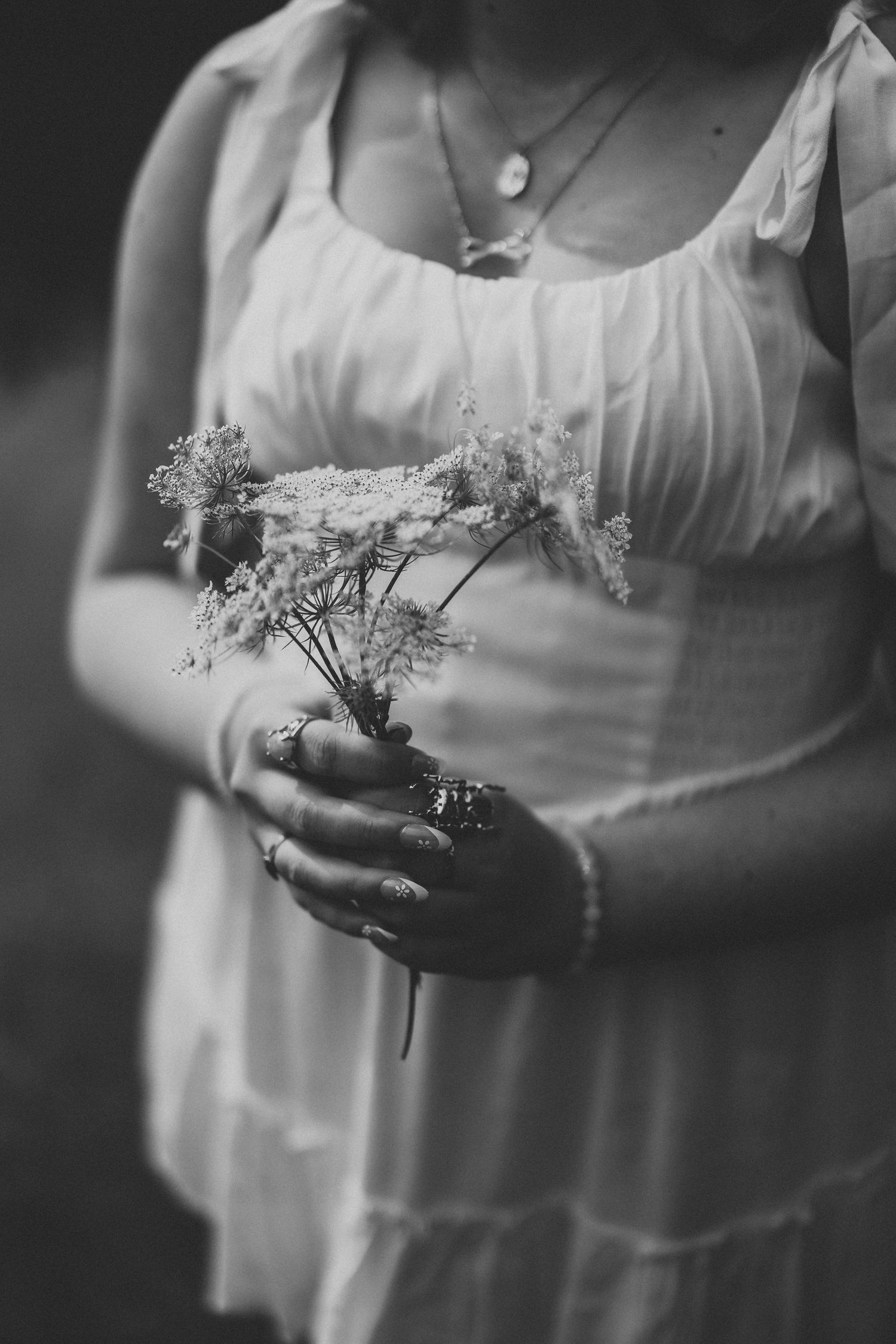 Delicate wildflowers held in hands wearing white dress, captured in black and white.