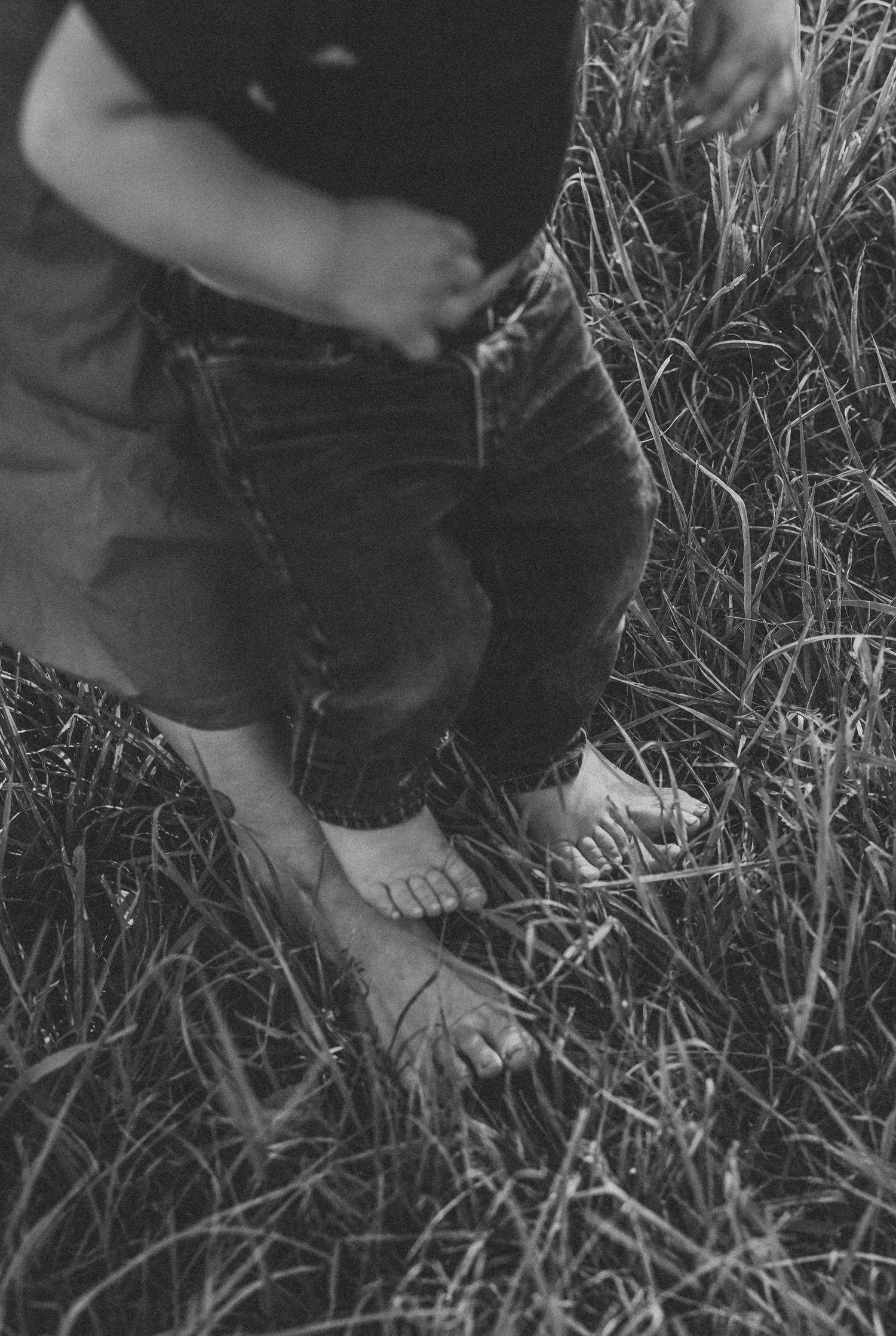 Black and white close-up of bare feet in tall grass.