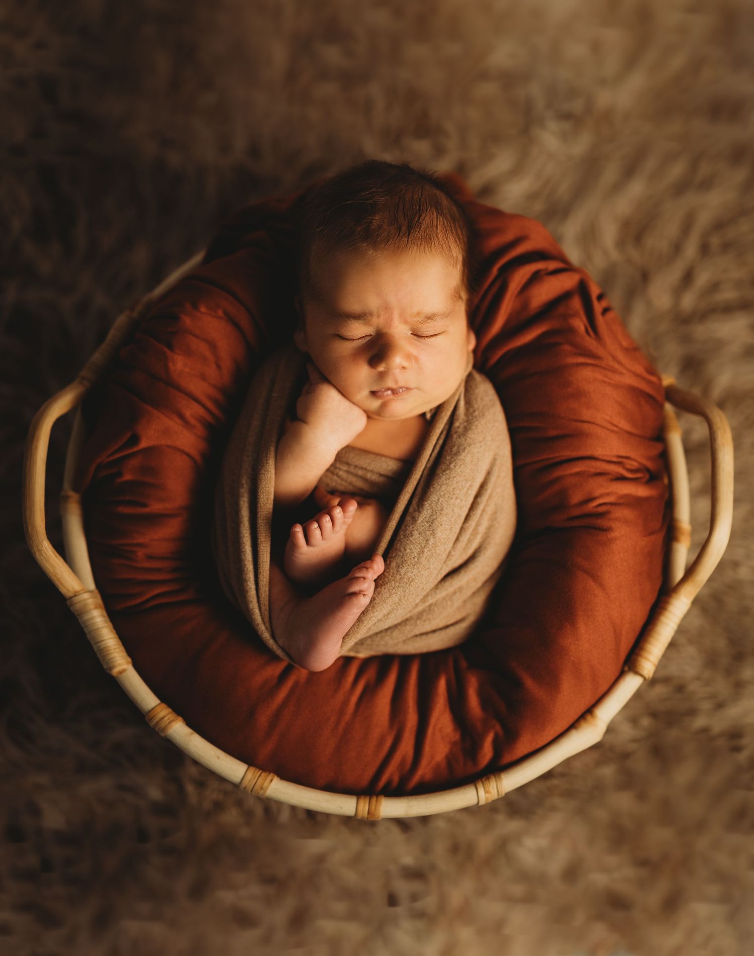 Sleeping newborn baby nestled in rustic basket with deep red fabric.