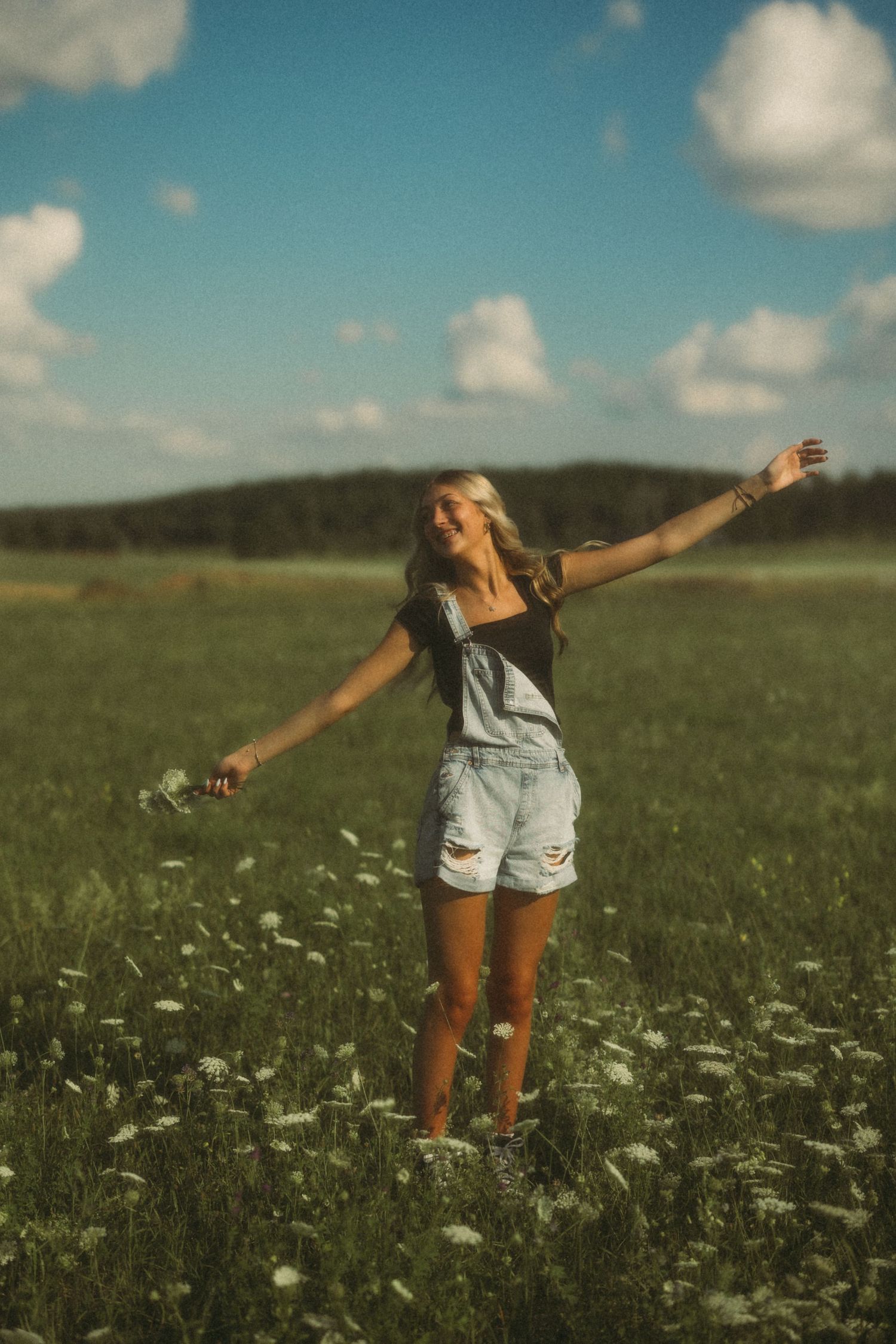 Someone spreading their arms joyfully in a field of daisies under a blue summer sky.