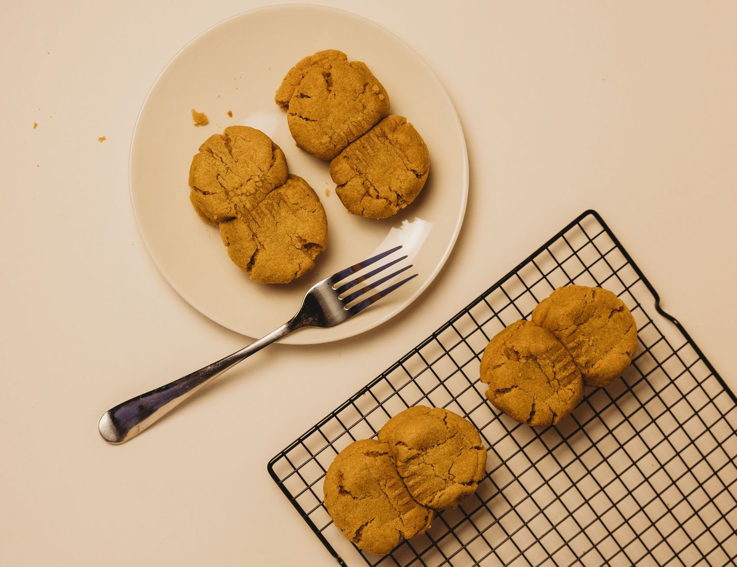 Golden peanut butter cookies on a white plate with a fork and cooling rack on a light background.