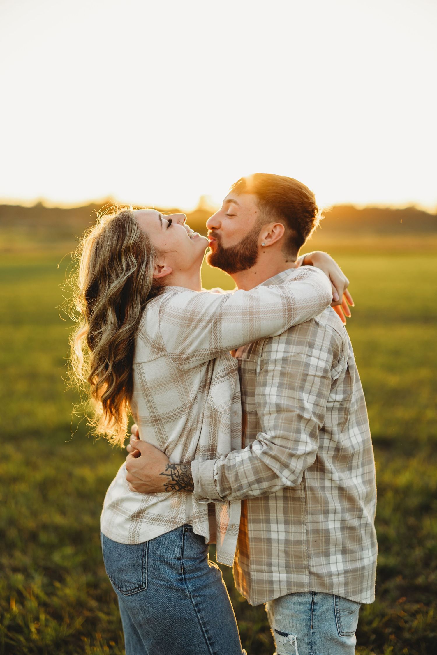 A couple embracing in a sunlit field wearing matching plaid shirts.