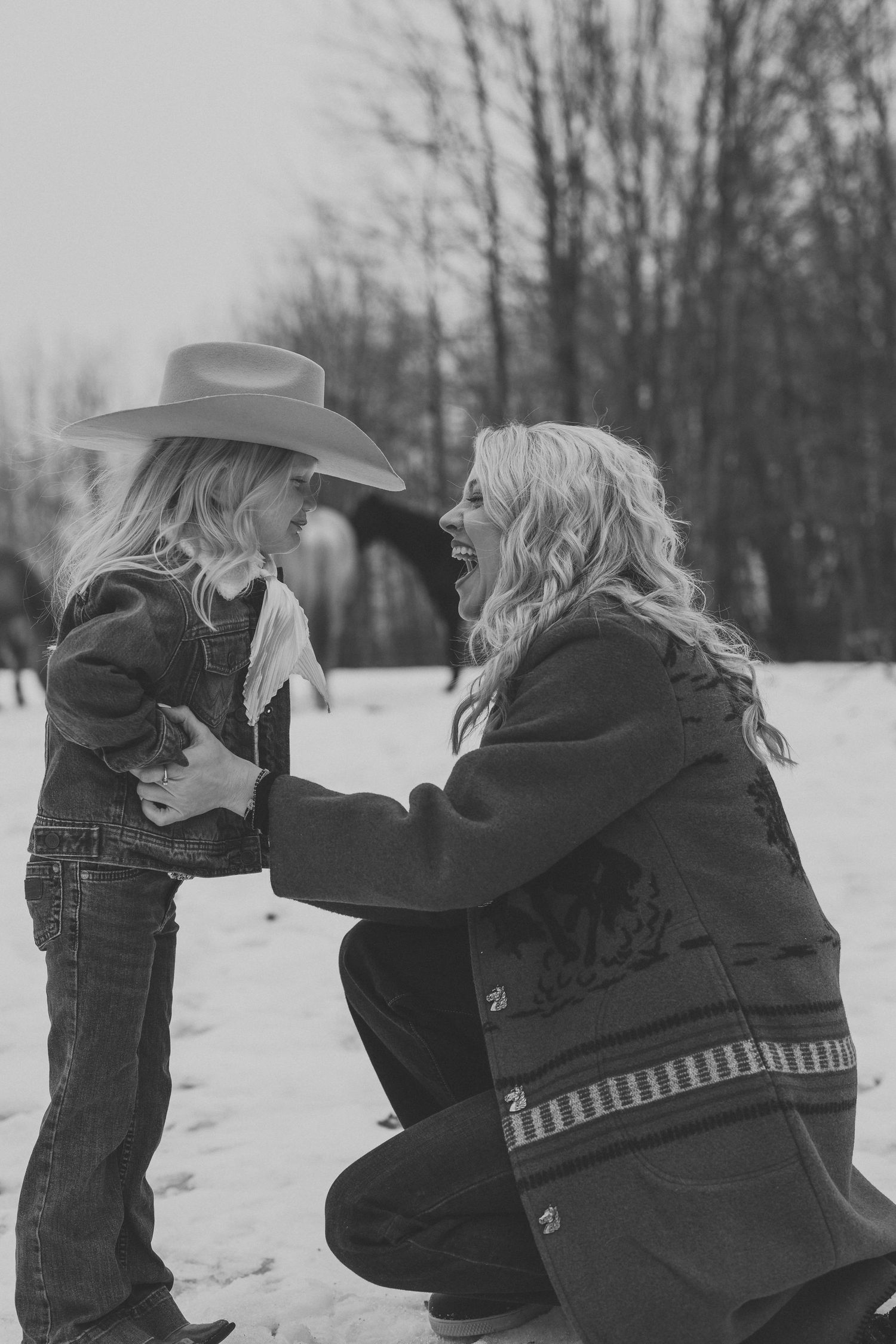 A tender winter moment between parent and child in the snow, with matching black coats and a cowboy hat.