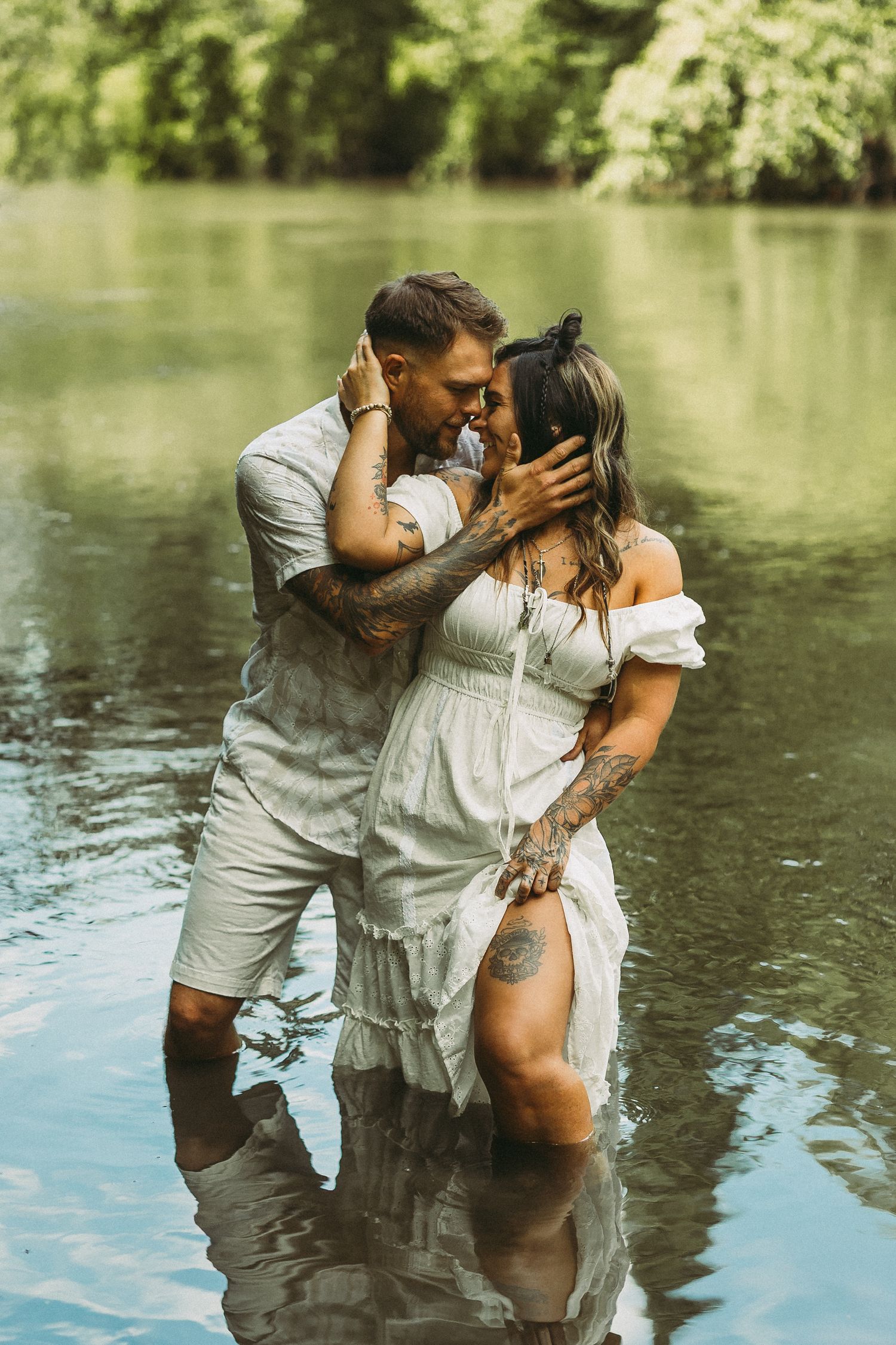 A romantic couple shares intimate moments while standing in a serene lake surrounded by greenery.