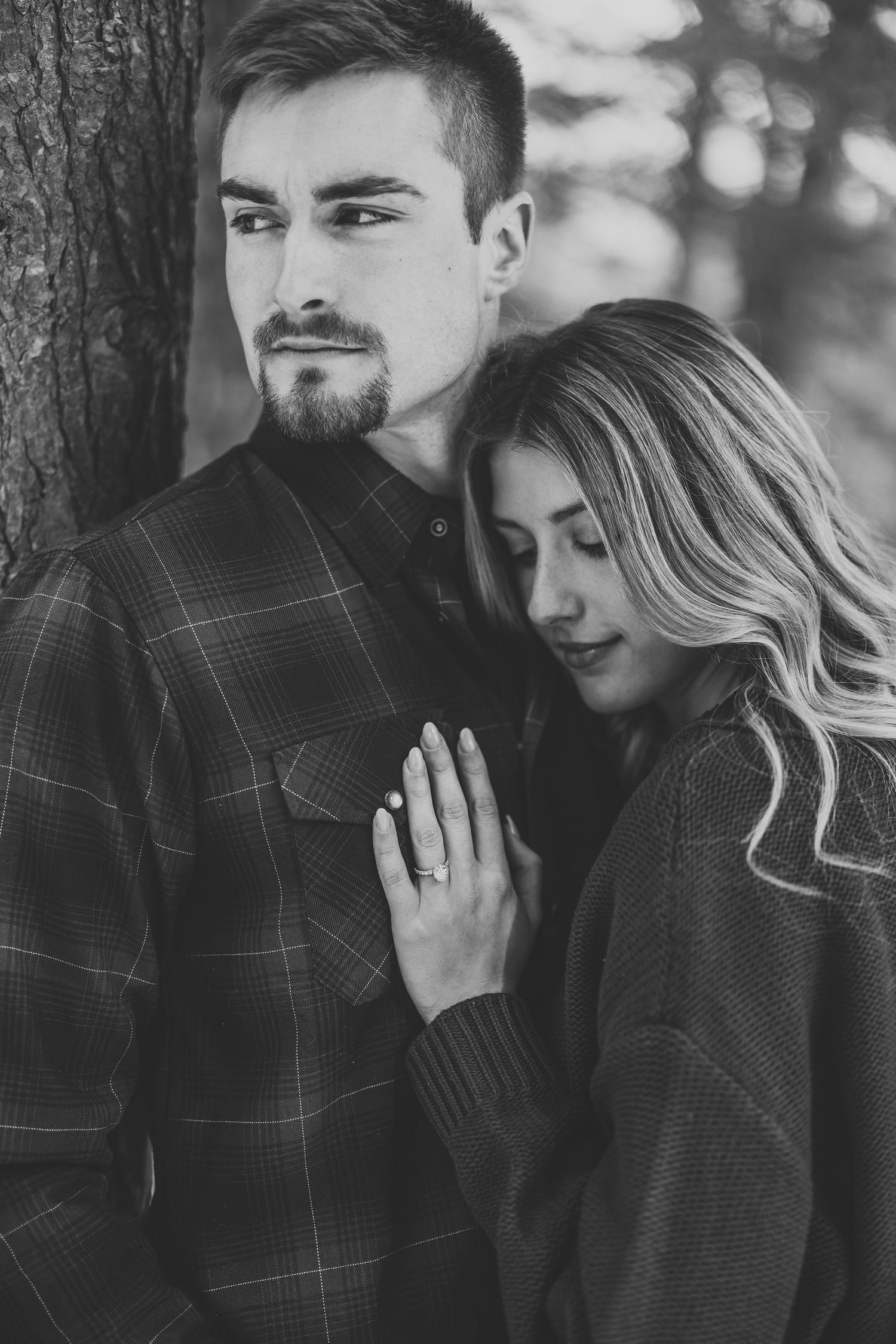 A romantic black and white photo series showing a couple embracing tenderly against a tree in a forest setting.