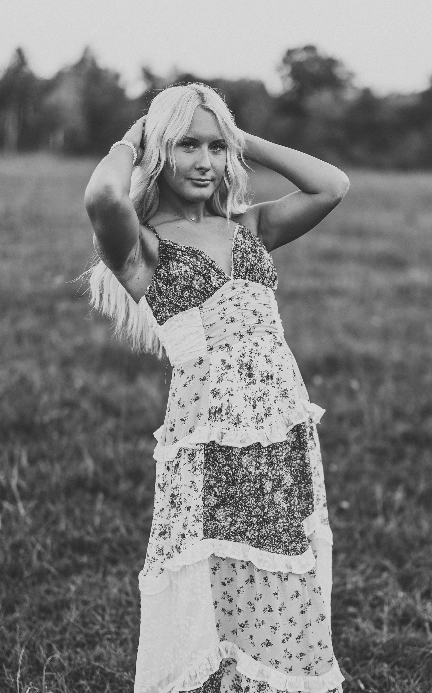 A person in a floral patterned dress poses in a field at sunset.