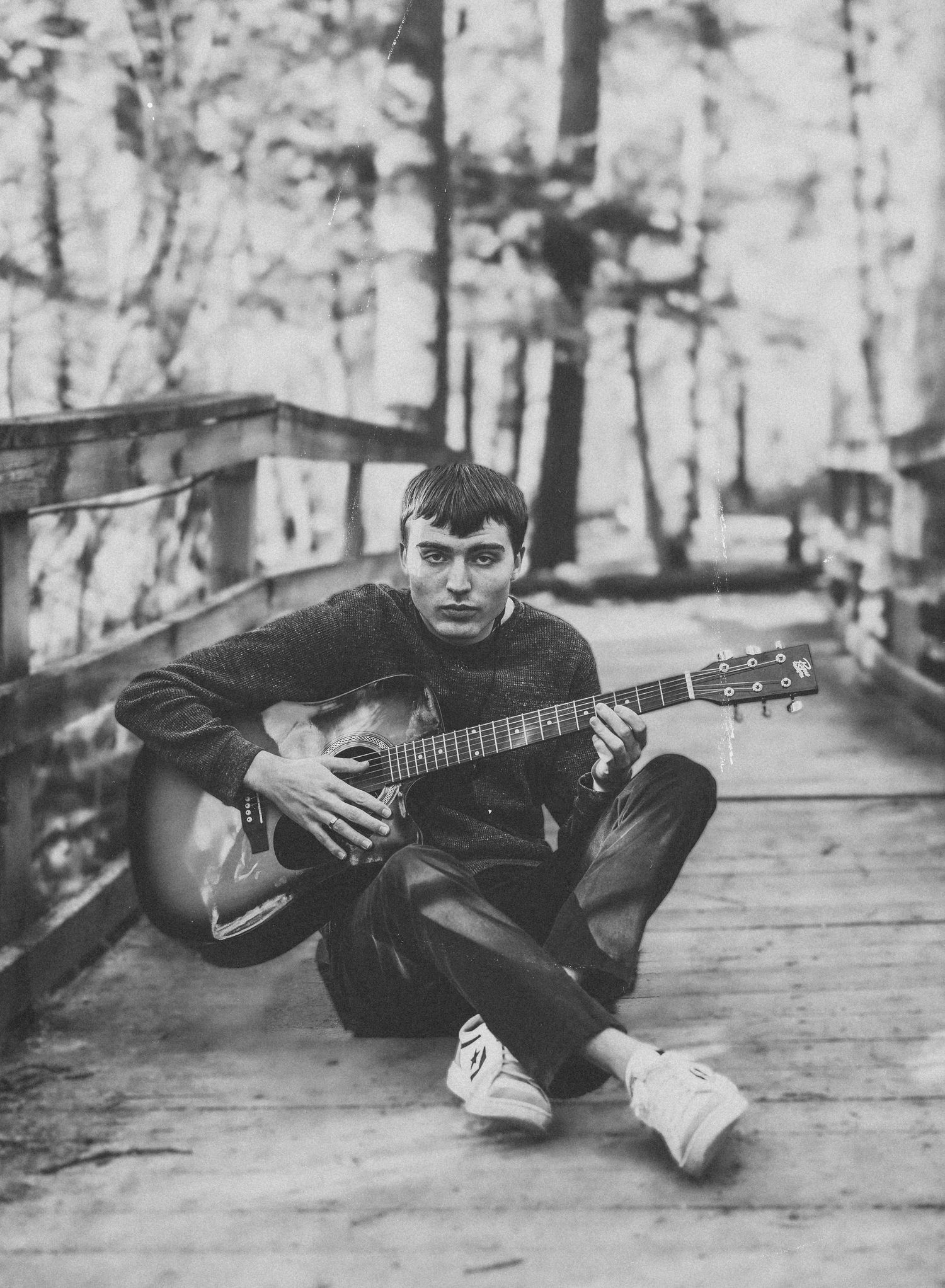 Guitar player lying down in various poses on wooden deck surrounded by trees.