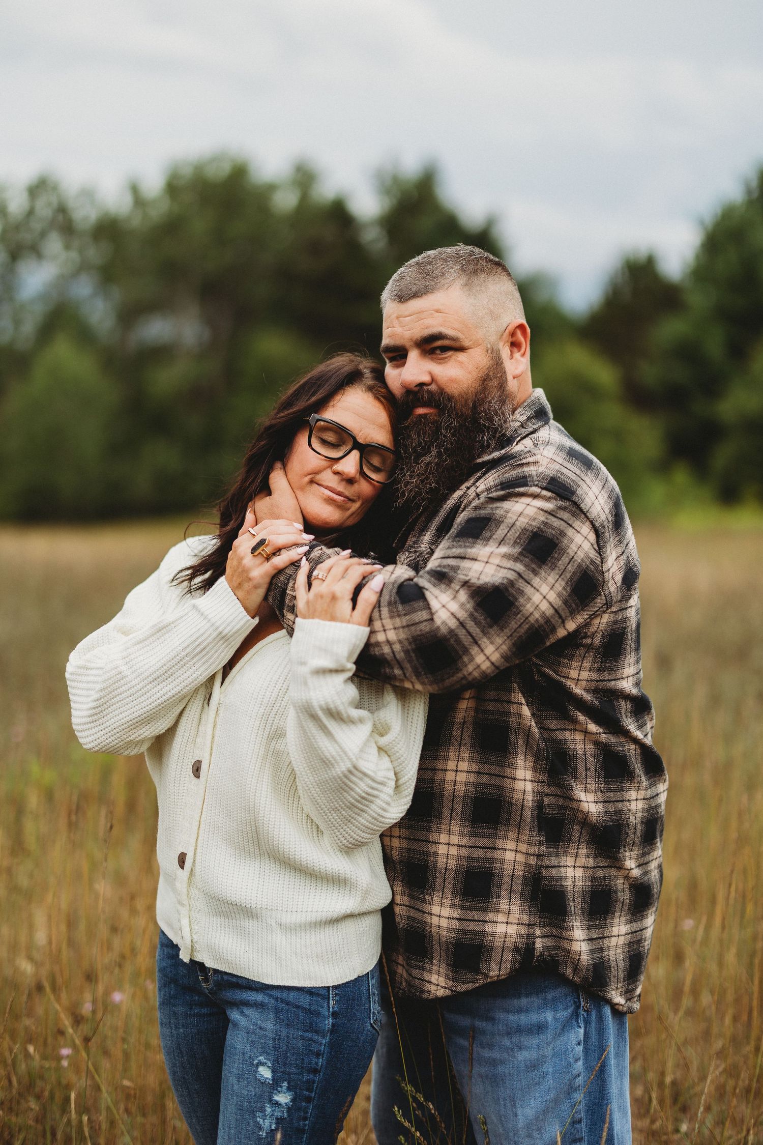 Playful couple in plaid shirt and white sweater sharing joyful moments in a field.