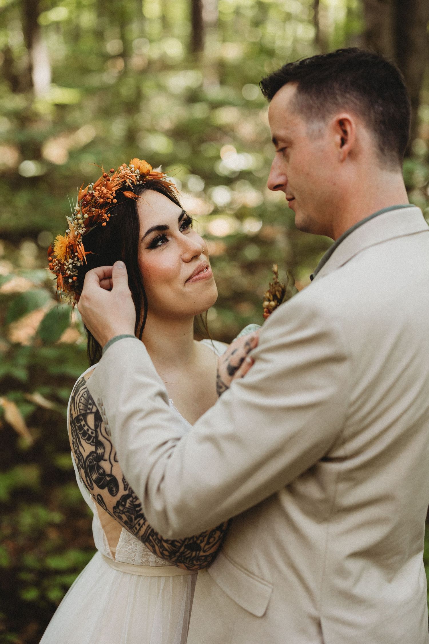 A couple shares an intimate moment in a forest setting during their wedding, with the bride wearing a floral crown.