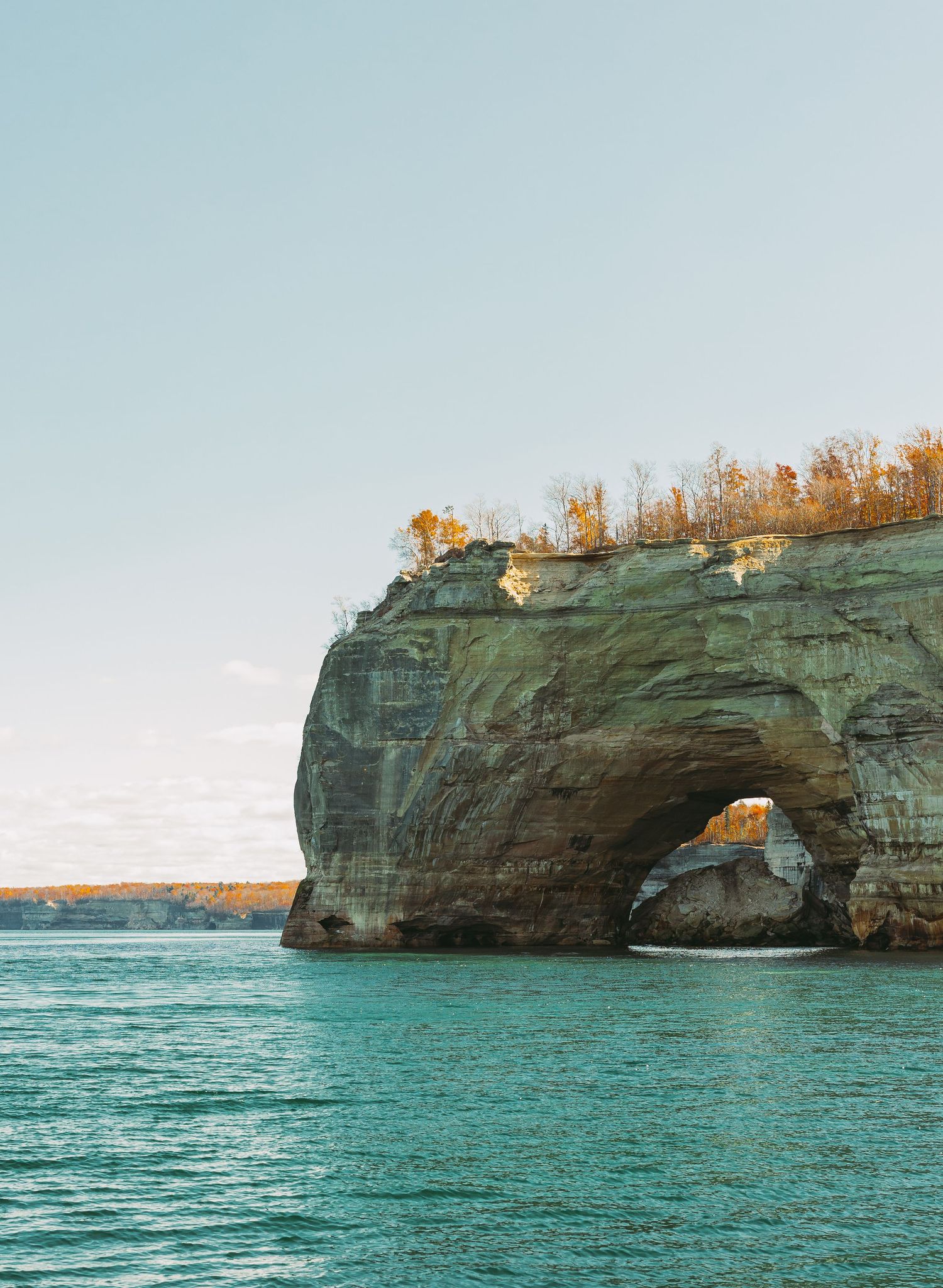 Natural stone arch formation in turquoise waters with rocky cliffs along the shoreline.