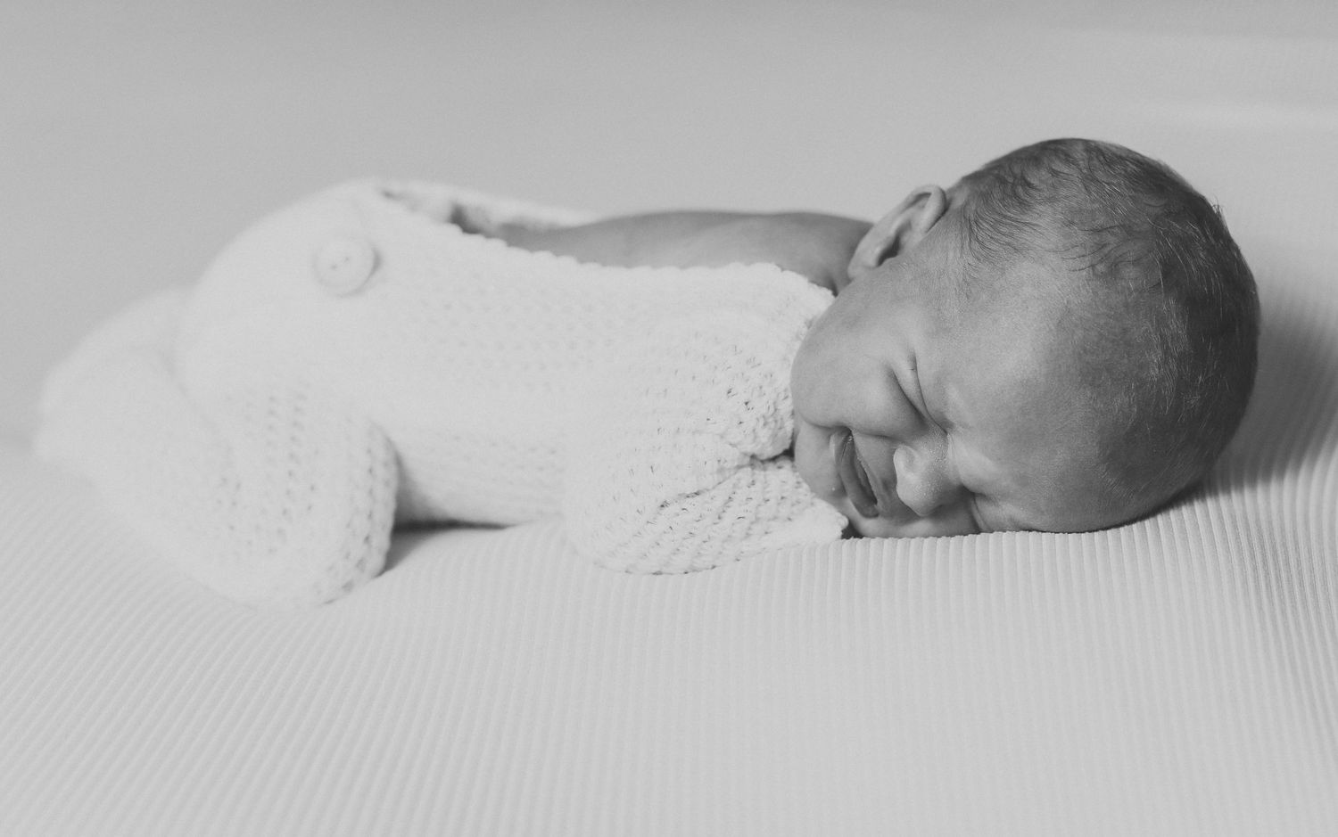 Black and white photo of a sleeping newborn baby wrapped in a white knit swaddle blanket.
