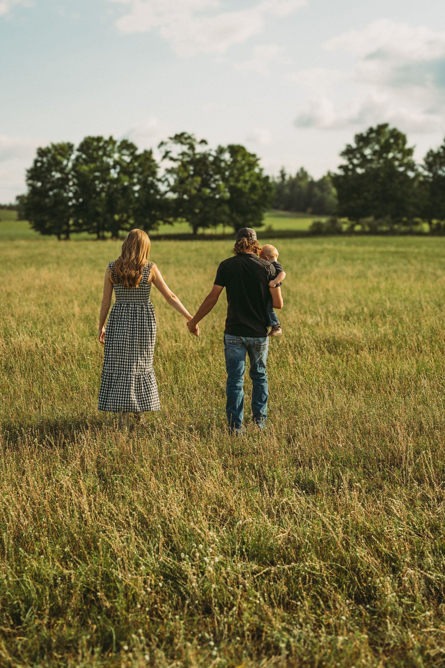 Family walking hand in hand through a scenic summer meadow with trees in the background.