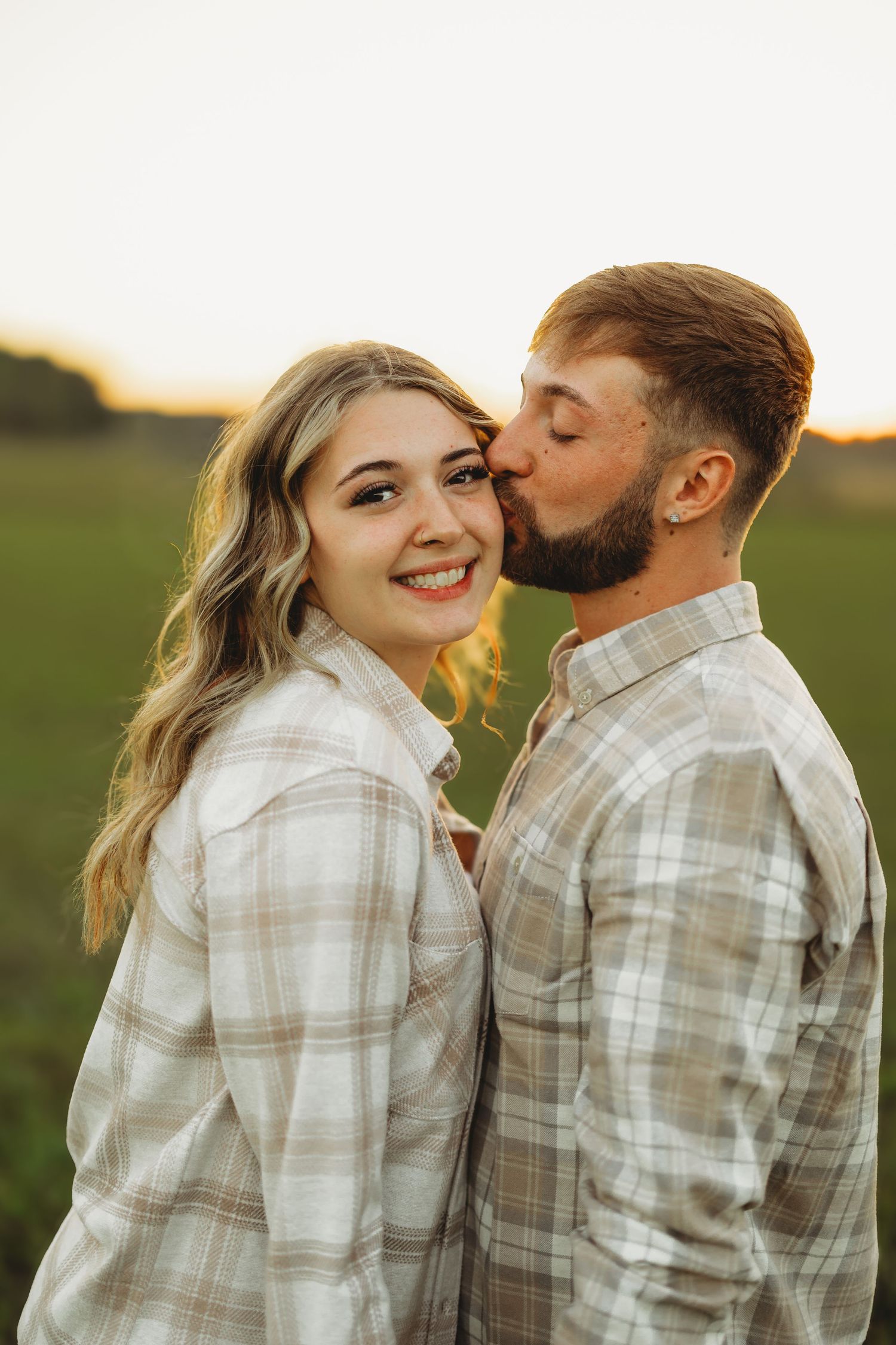 Intimate couple sharing tender moments in a field wearing matching plaid shirts.