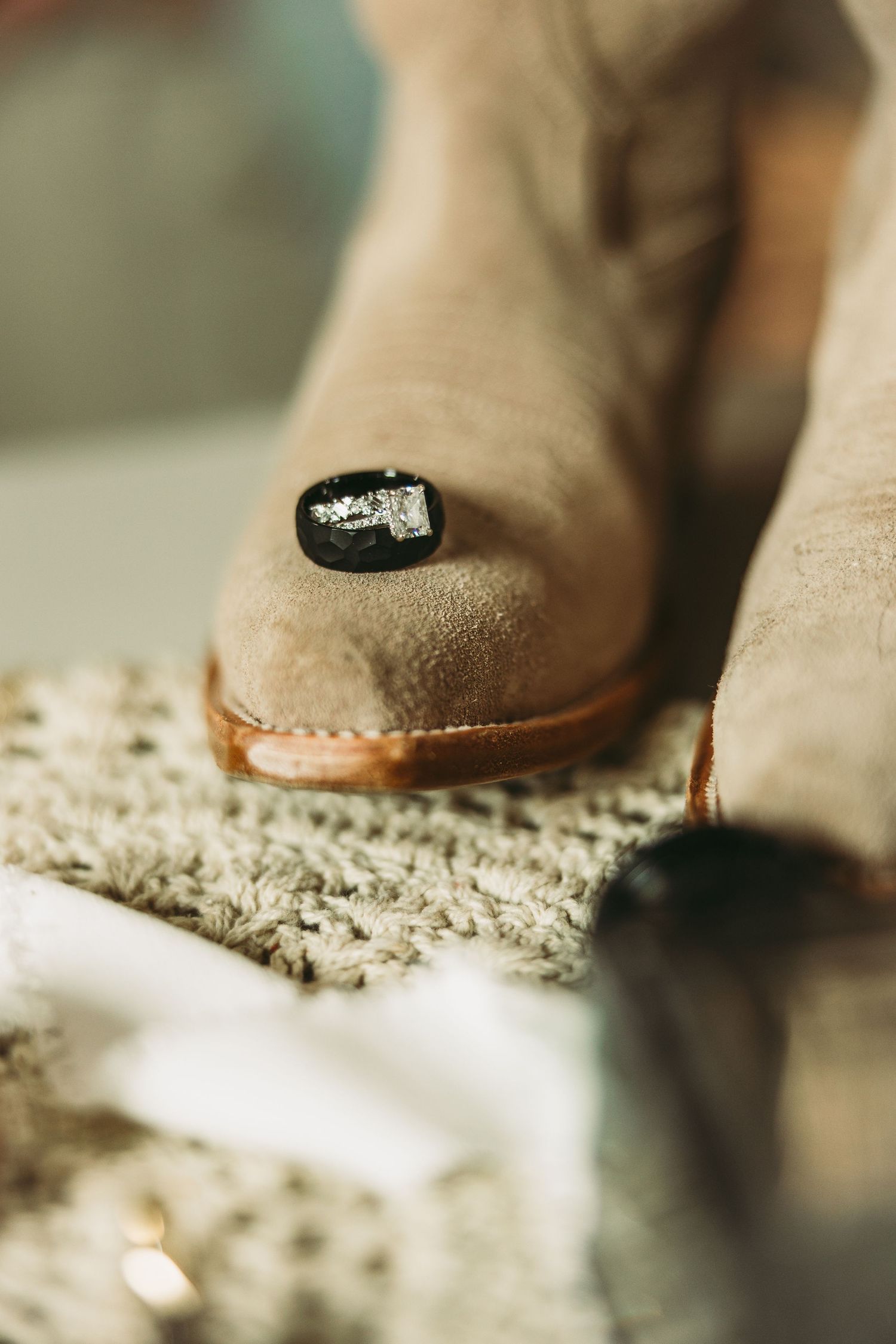 Close-up of engagement ring sparkling against beige suede boots.