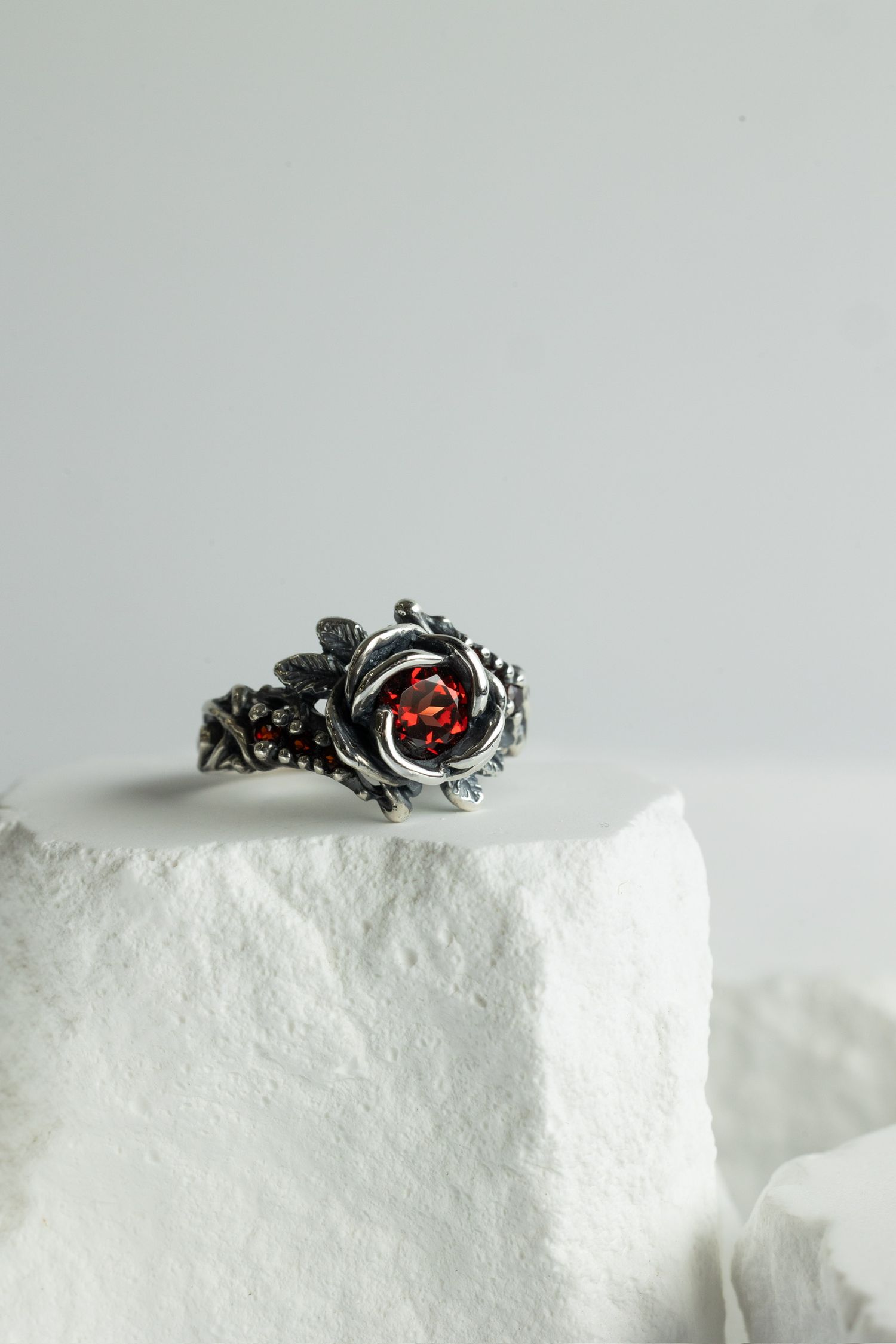 Gothic style silver ring with red stone in detailed floral setting on white background.