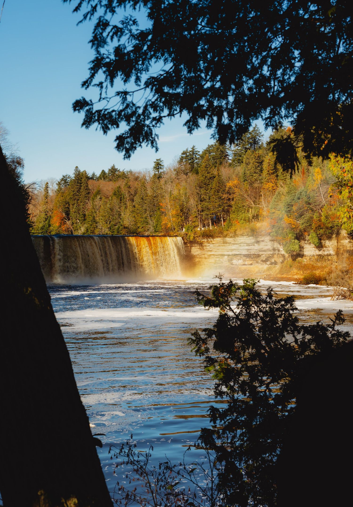 Dramatic waterfall with white rapids surrounded by fall foliage and evergreen trees.
