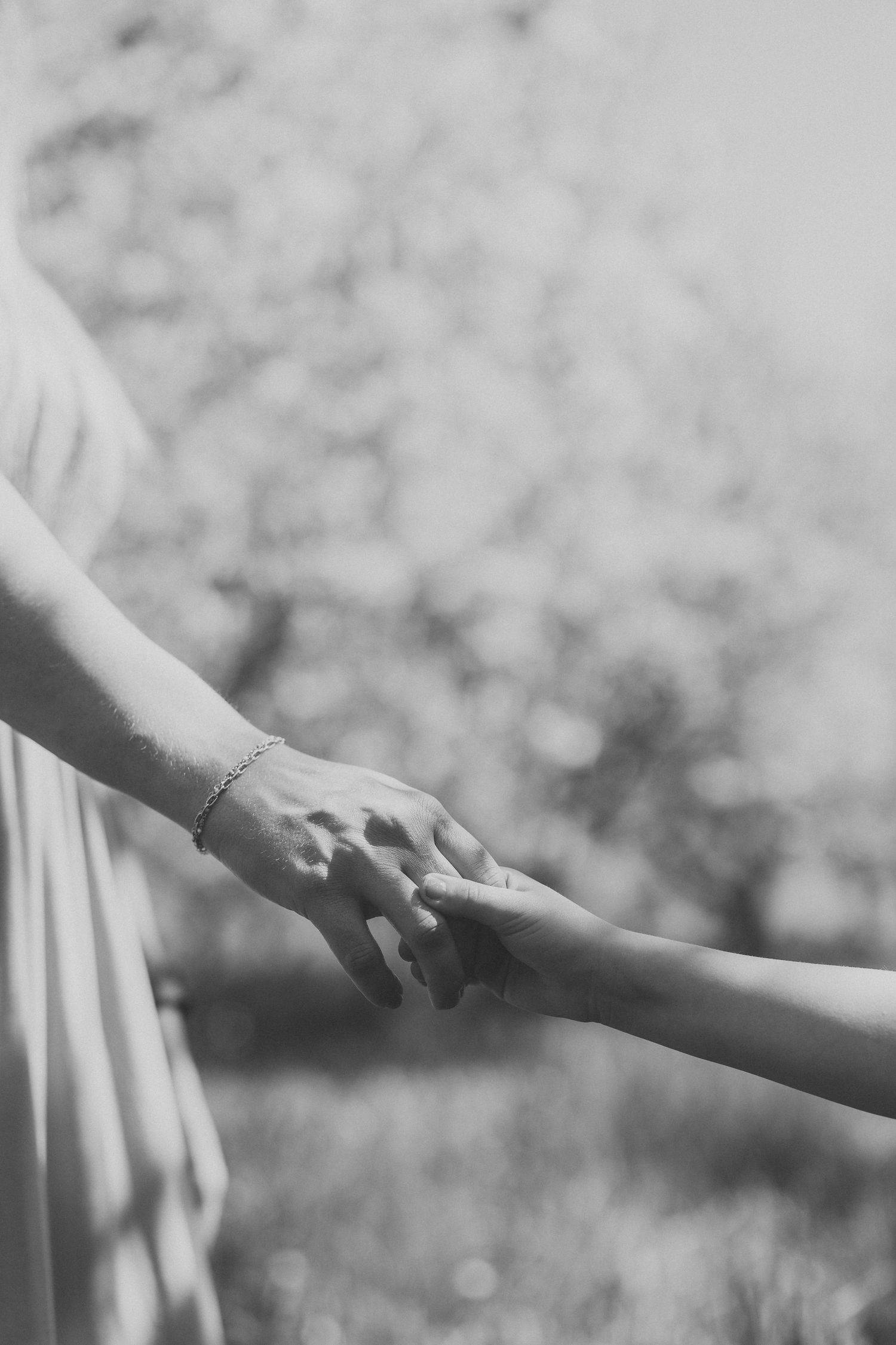 Black and white photo of two people gently holding hands outdoors, with a bracelet visible on one wrist.