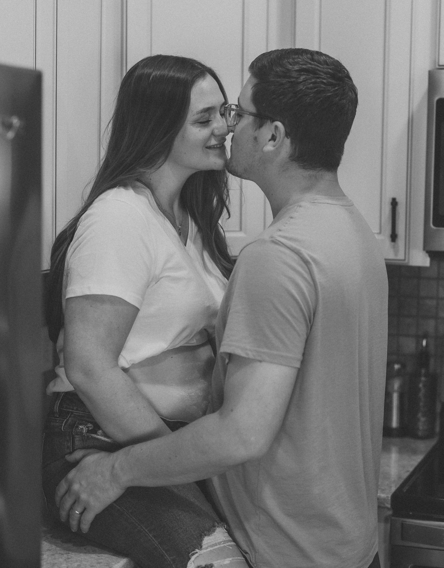 Black and white photo of a couple sharing a romantic moment in a kitchen, leaning in for a kiss.